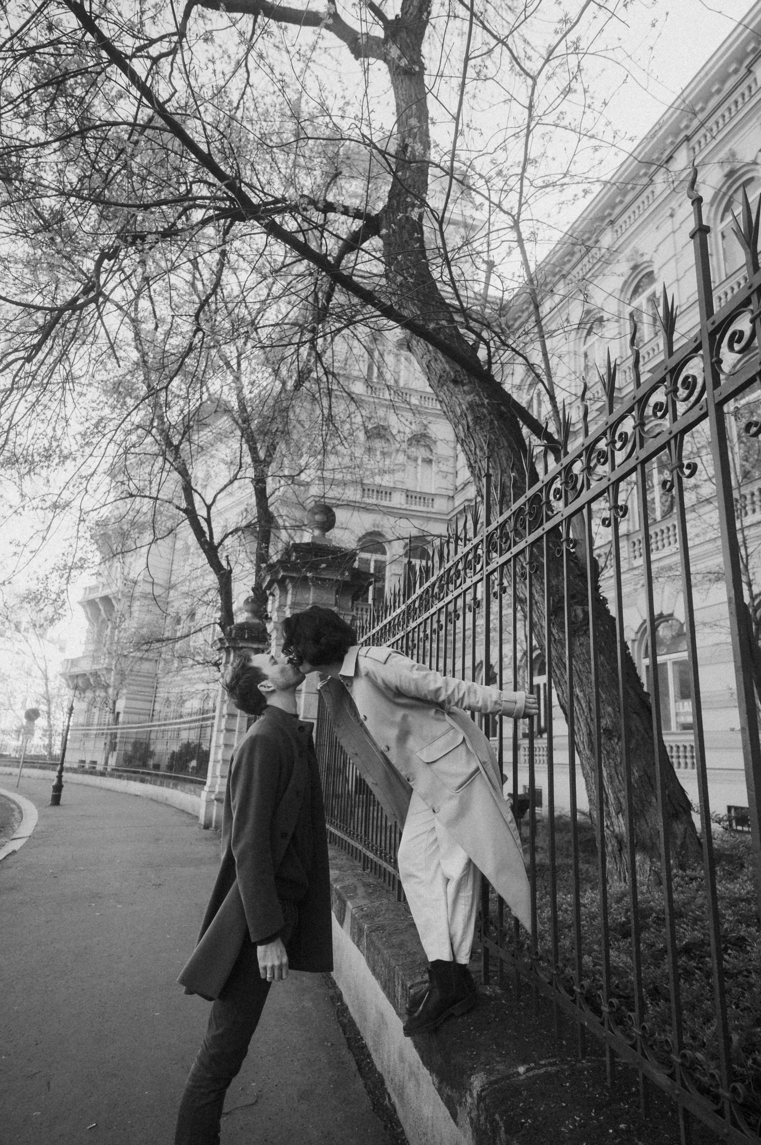 Black and white photos show two people in theatrical poses against a vintage architectural backdrop with iron gates.