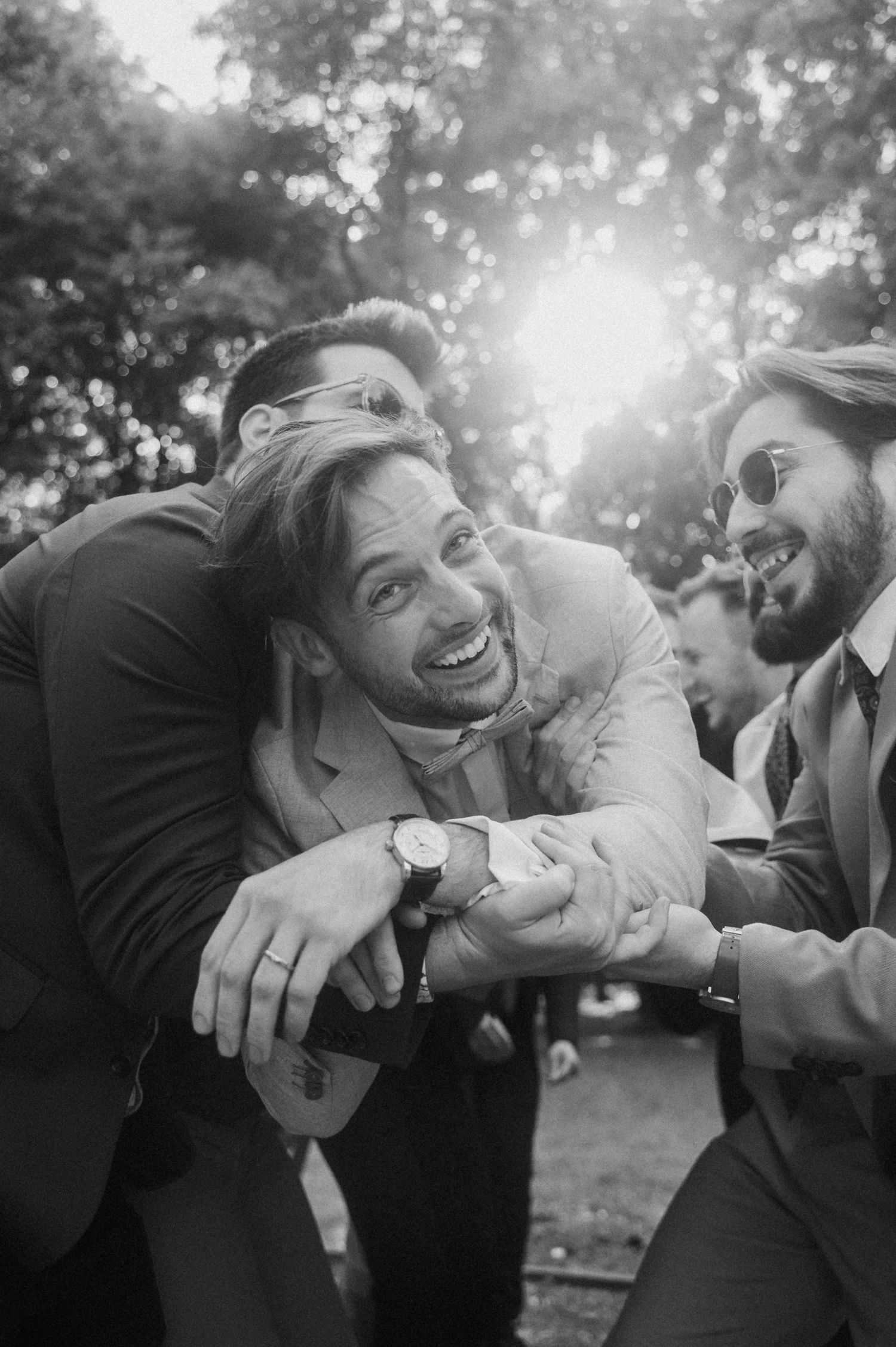 A candid black and white photo capturing joyful laughter between friends outdoors with sunlight filtering through trees.
