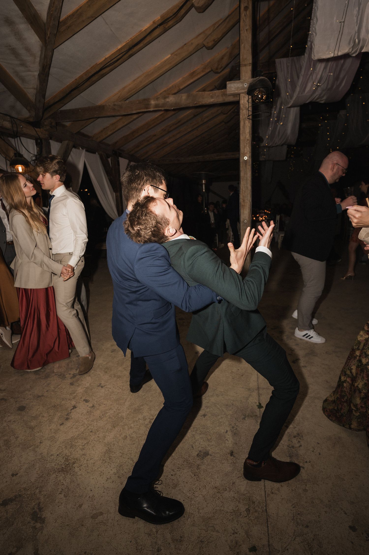 Two photographers in a rustic barn setting crouch low to capture shots from different angles during an event.