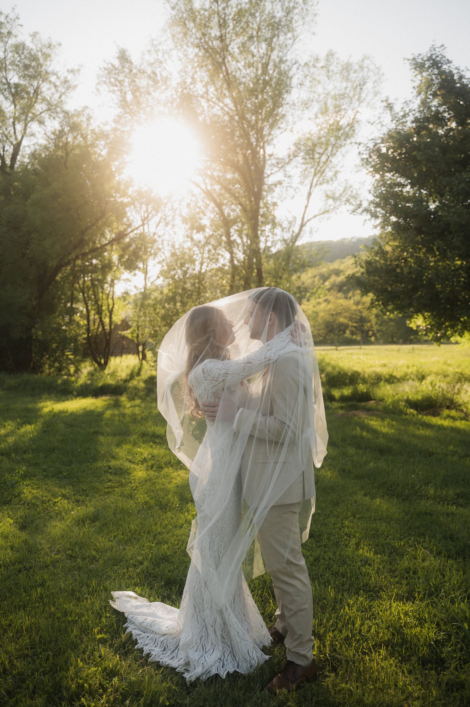 A couple in white clothing dances together in a sunlit meadow at golden hour.
