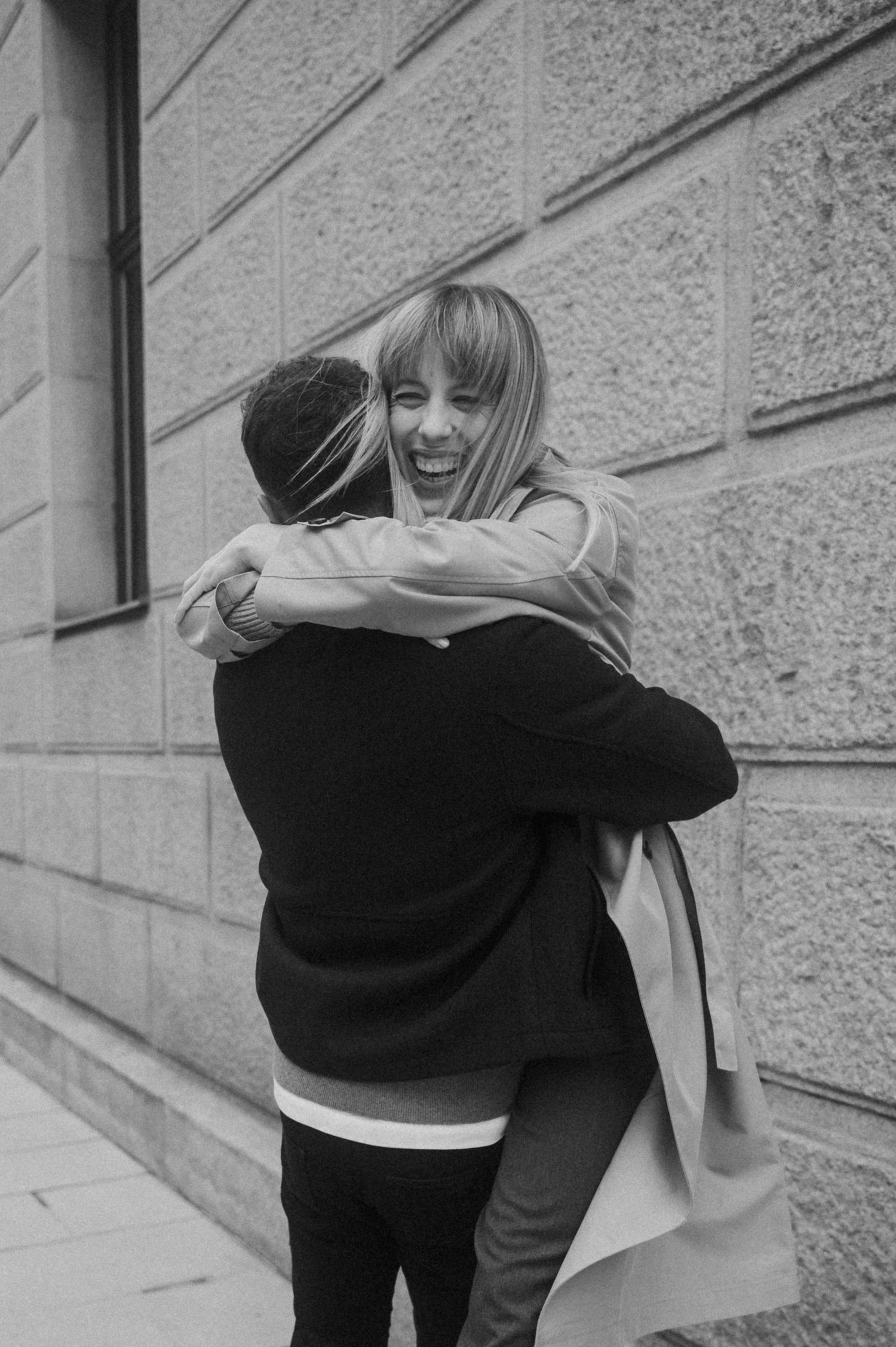 A black and white photo sequence shows two people embracing in a warm hug against a textured wall.