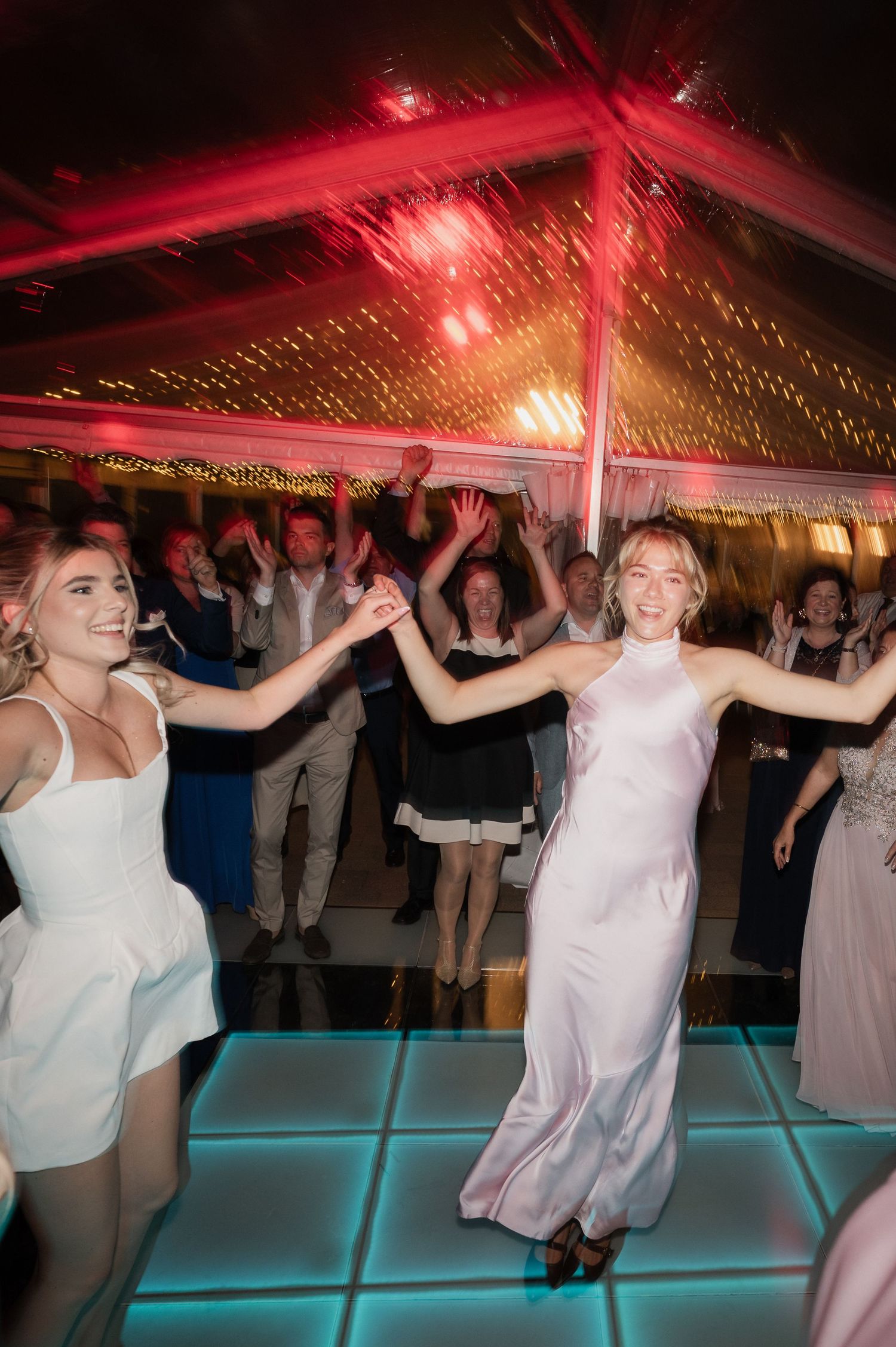 Bride dancing joyfully with guests under colorful lights at a lively wedding reception party.