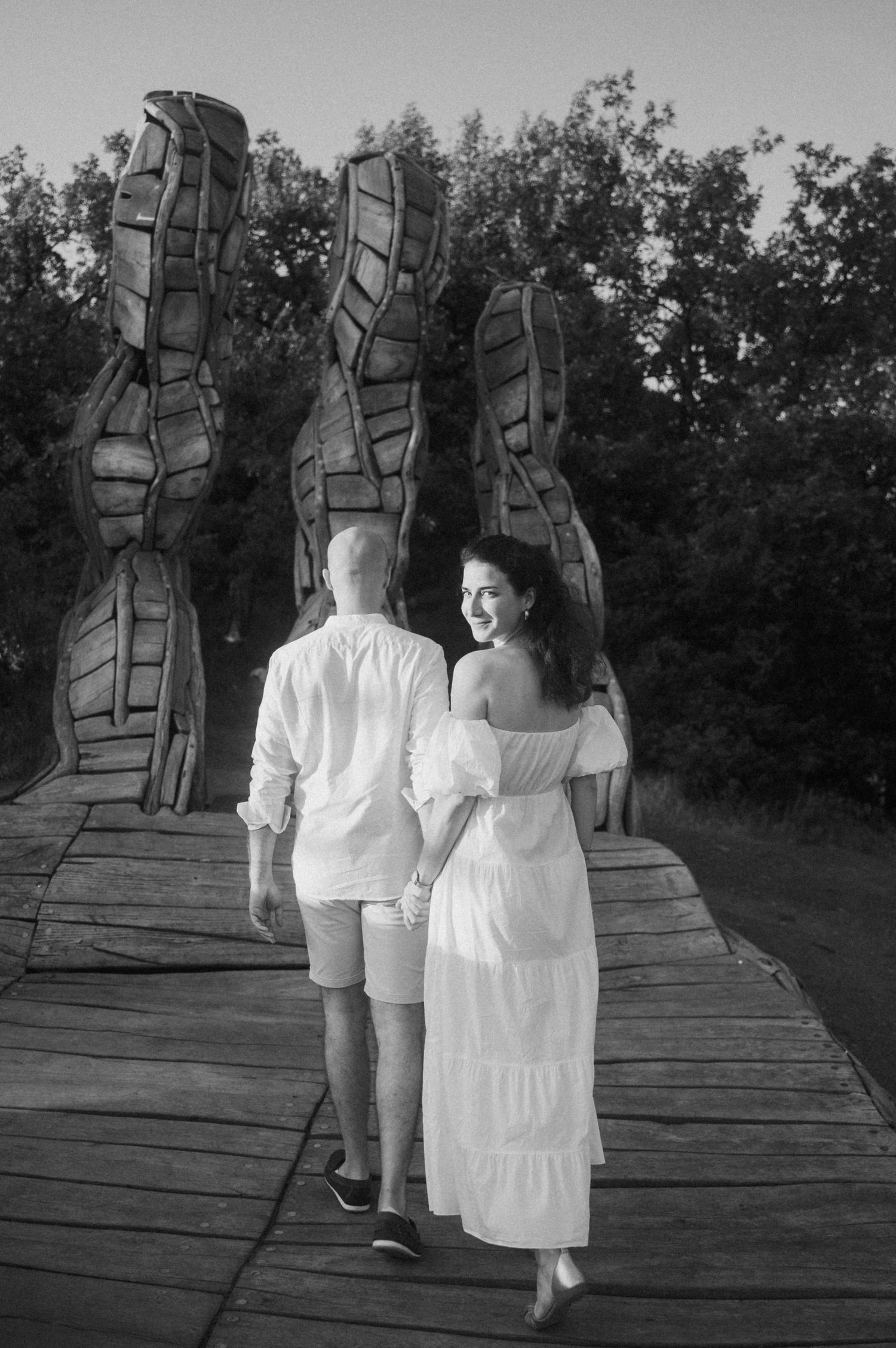 A couple walks together on a wooden bridge in a black and white photo series showing progression of their movement.