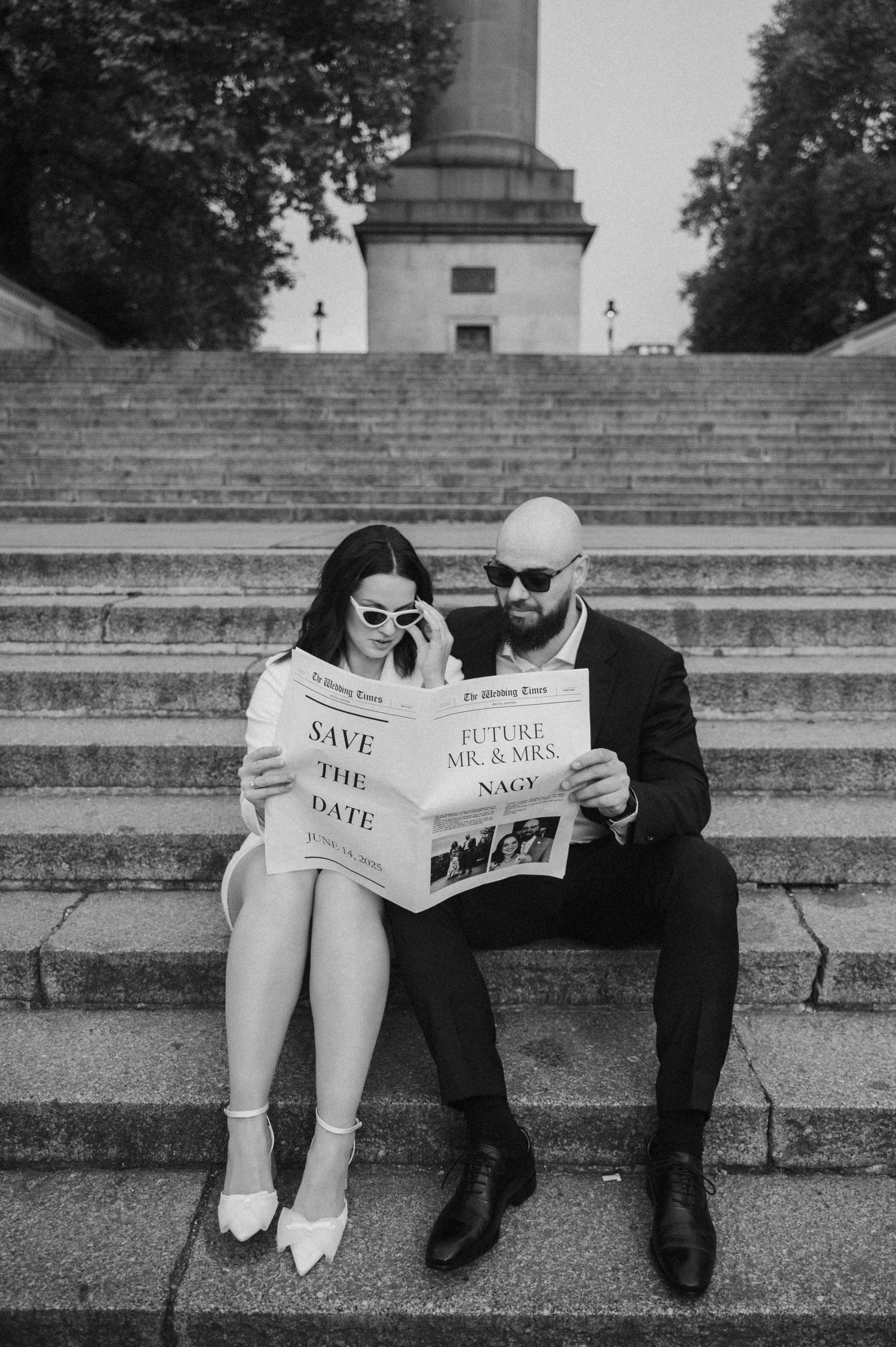 A couple sits on stone steps reading newspapers in a creative engagement photo.