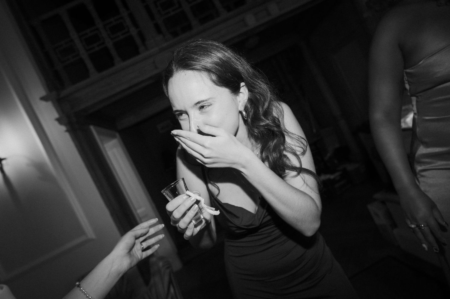 A woman covers her mouth in surprise during a wedding reception in this candid black and white photo.