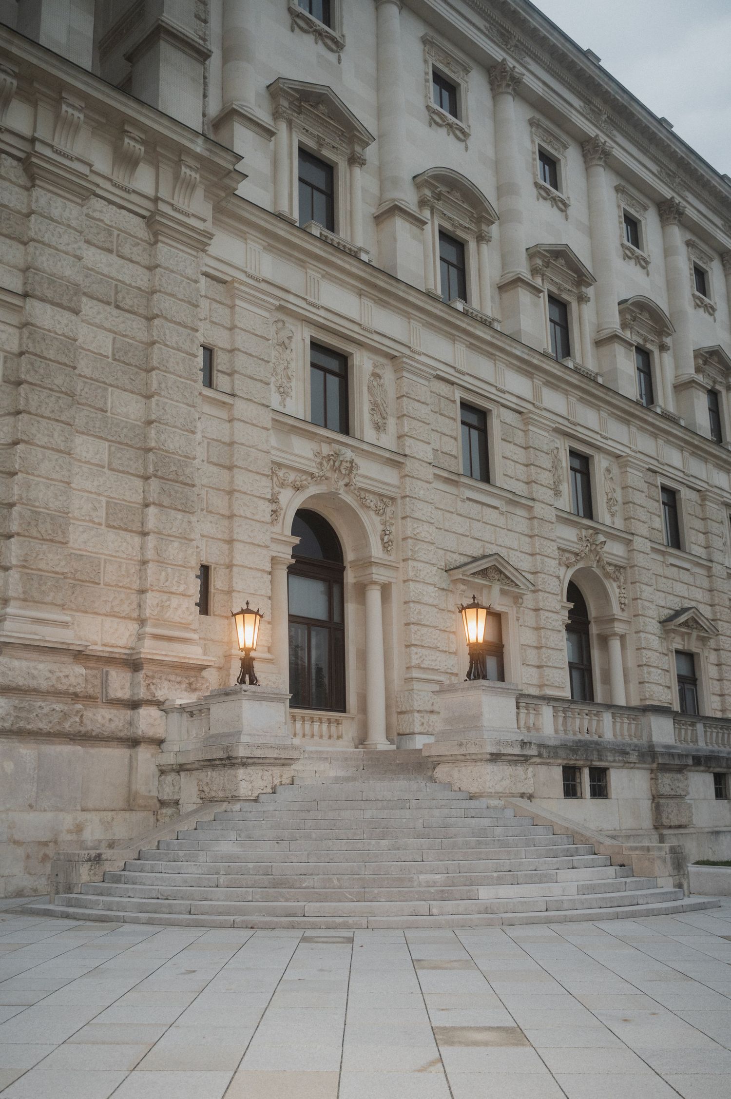 Three views of ornate stone steps leading to a grand historic building entrance with illuminated wall lamps.