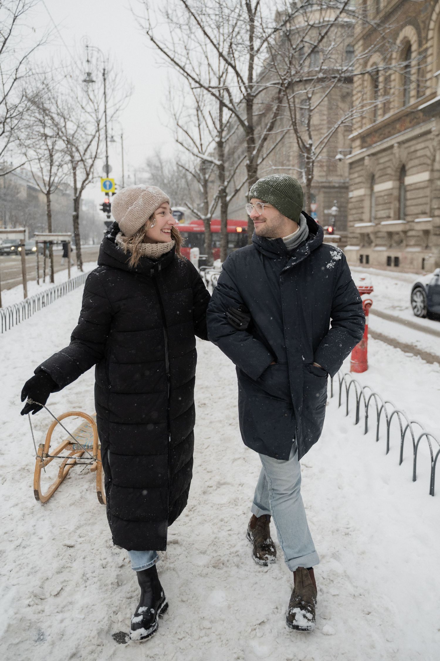Two people in winter coats playing in the snow near an ornate building.