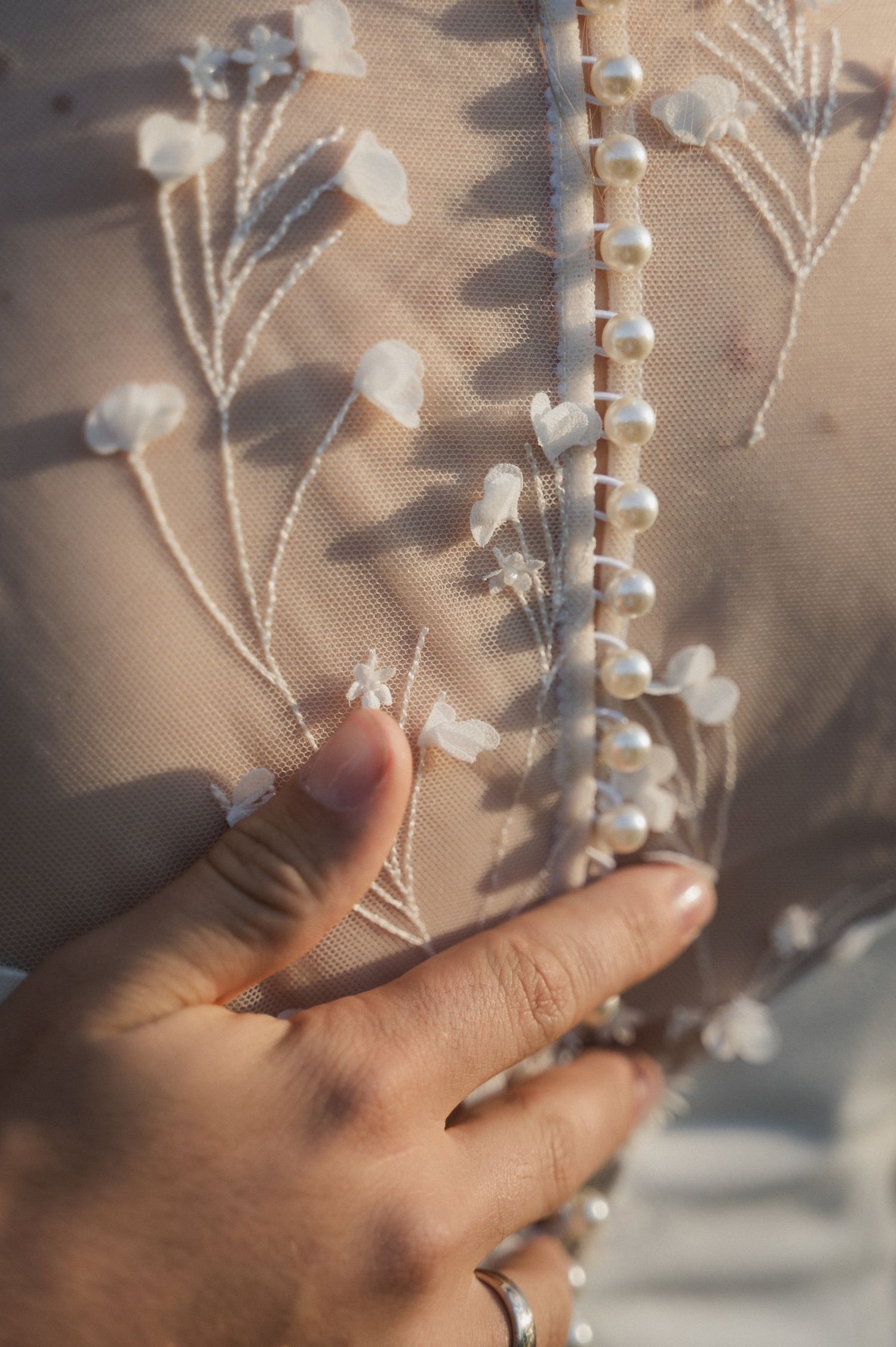 A hand gently touches delicate white floral lace fabric against a soft beige background.