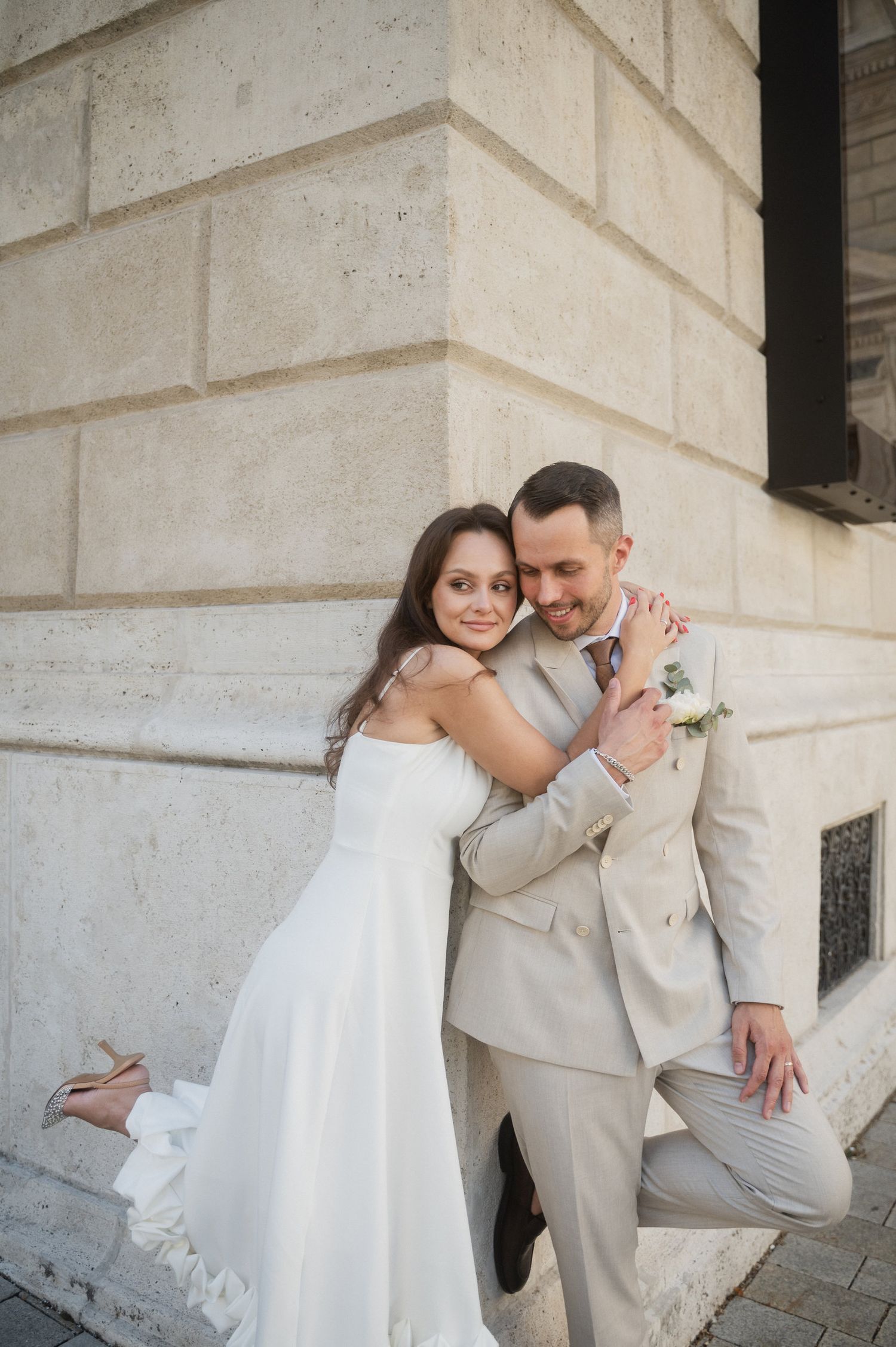 Romantic wedding portraits against light stone wall showing playful interactions.