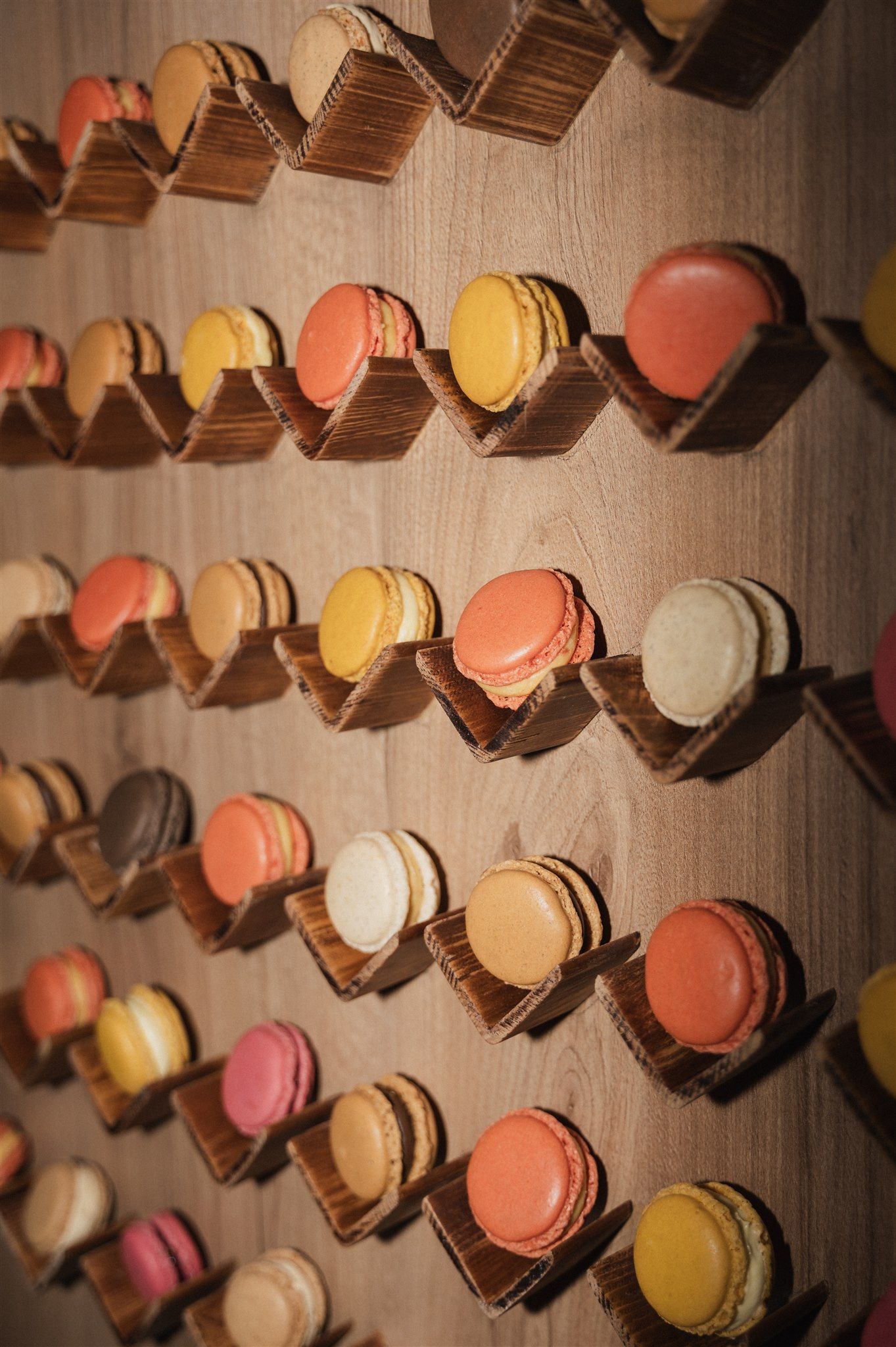 Colorful macarons displayed on a wooden wall in rows casting dramatic shadows.