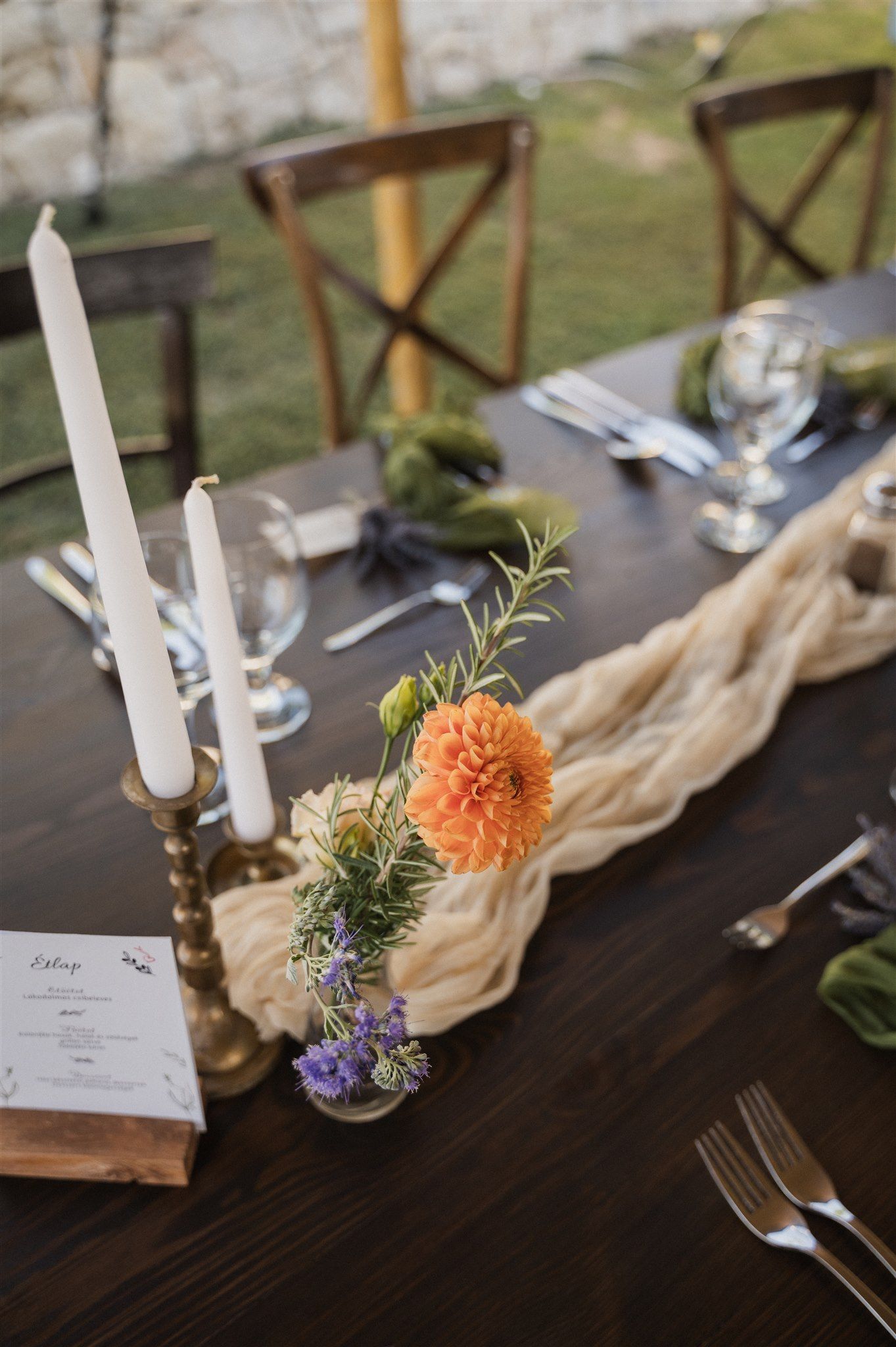 Wedding table decor featuring orange flowers, white candles, and delicate table settings.