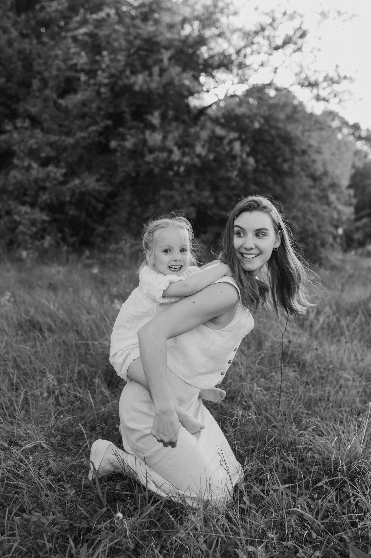 Black and white portrait of a mother and child sharing a joyful moment together in a grassy outdoor setting.