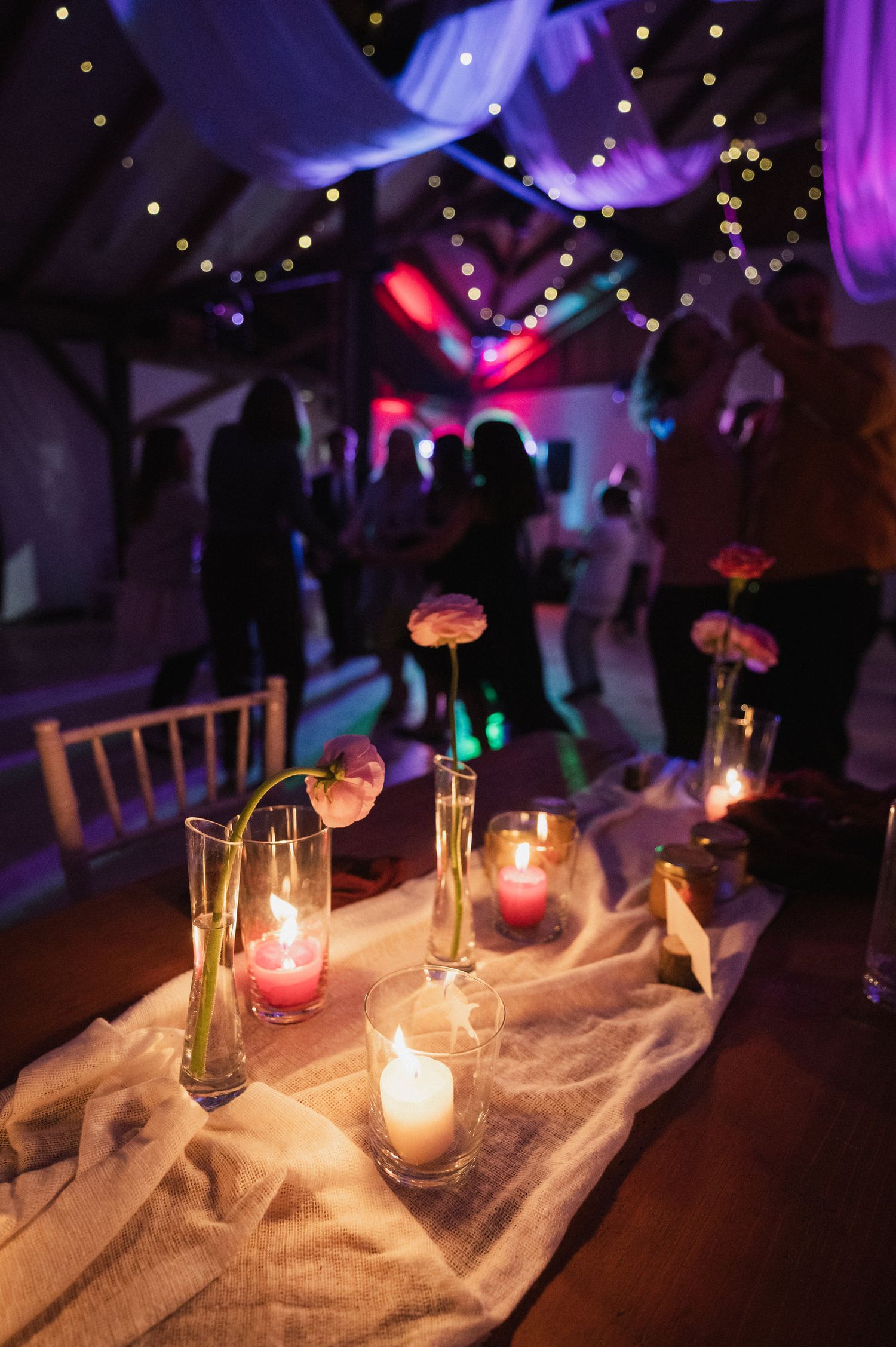 Glowing candles in glass holders create romantic ambiance on a white tablecloth at an evening event.