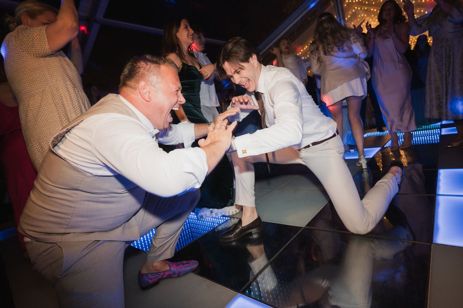 Two guests playfully posing on a reflective dance floor during a festive wedding reception celebration.