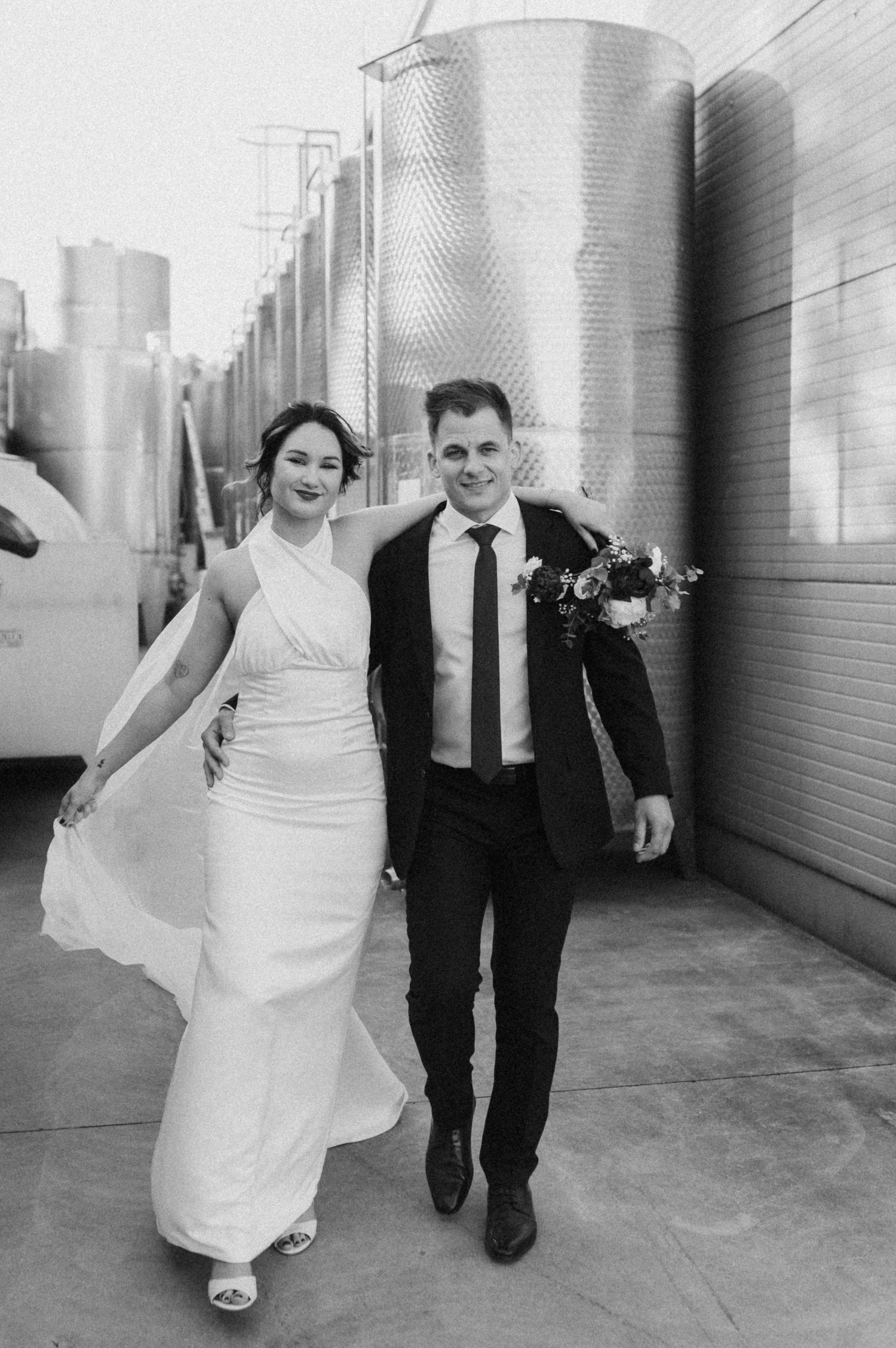 Black and white wedding photo series showing couple walking together through an industrial hallway with metal tanks.