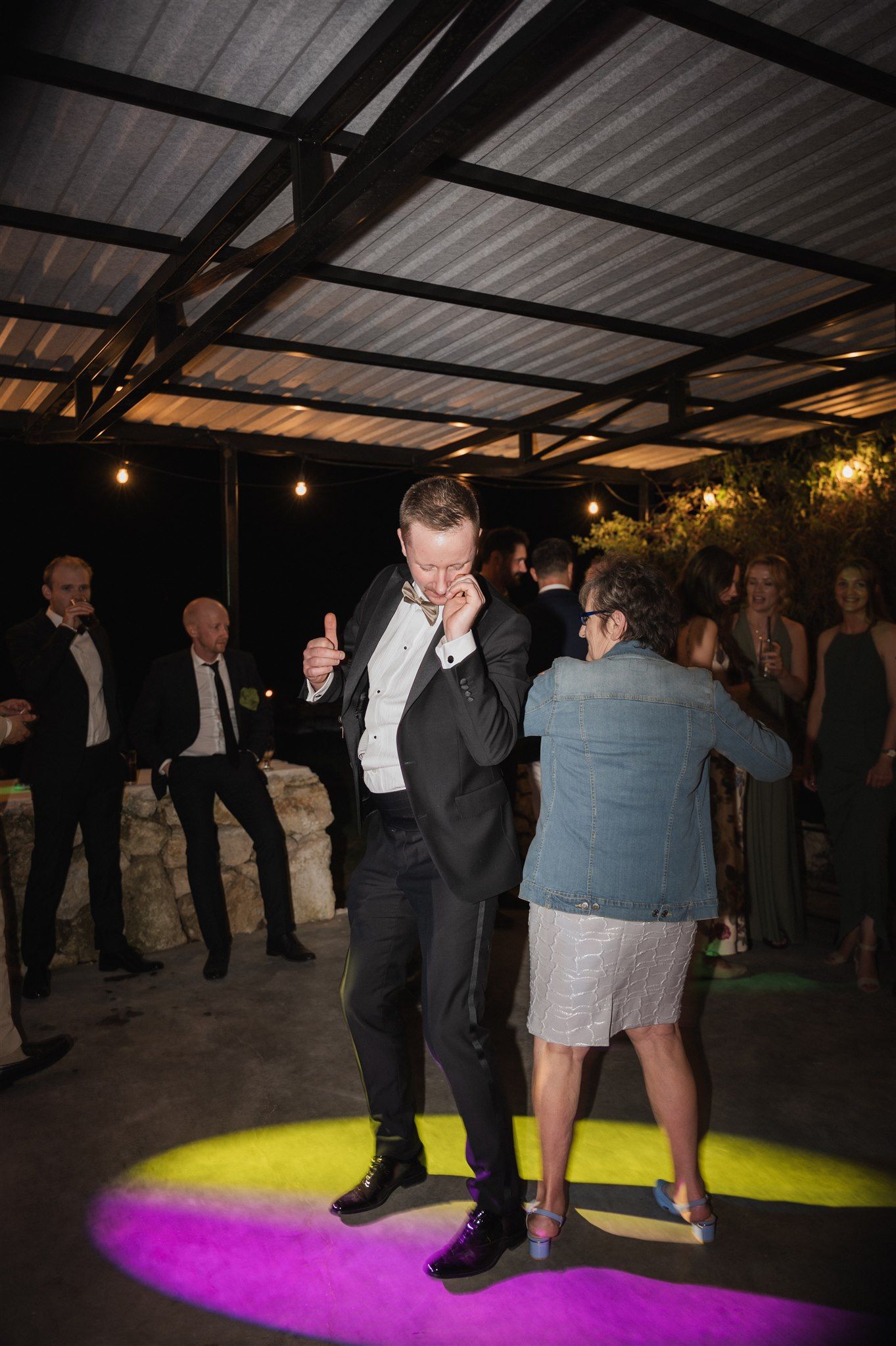 Wedding guests dancing on illuminated floor with purple and yellow lighting effects.