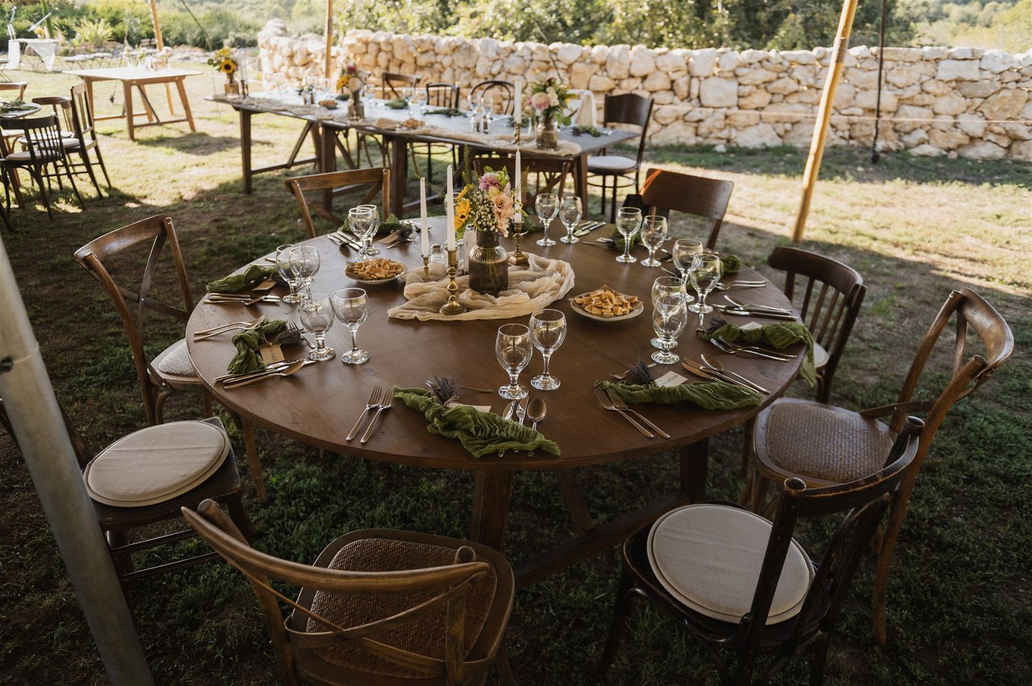 Outdoor wedding reception setup with rustic tables and chairs under shade.