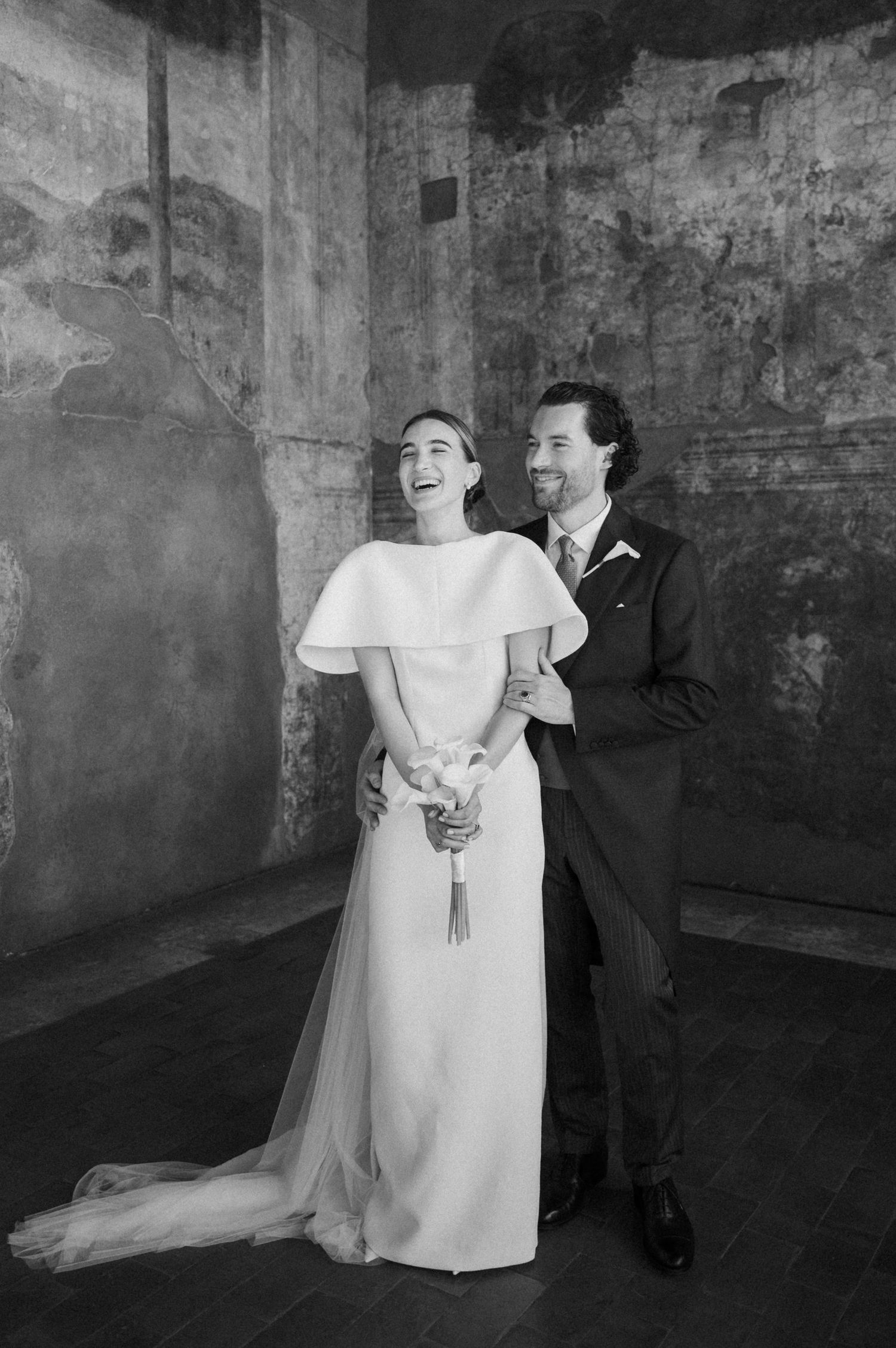 Joyful wedding couple dancing in a historic stone venue.