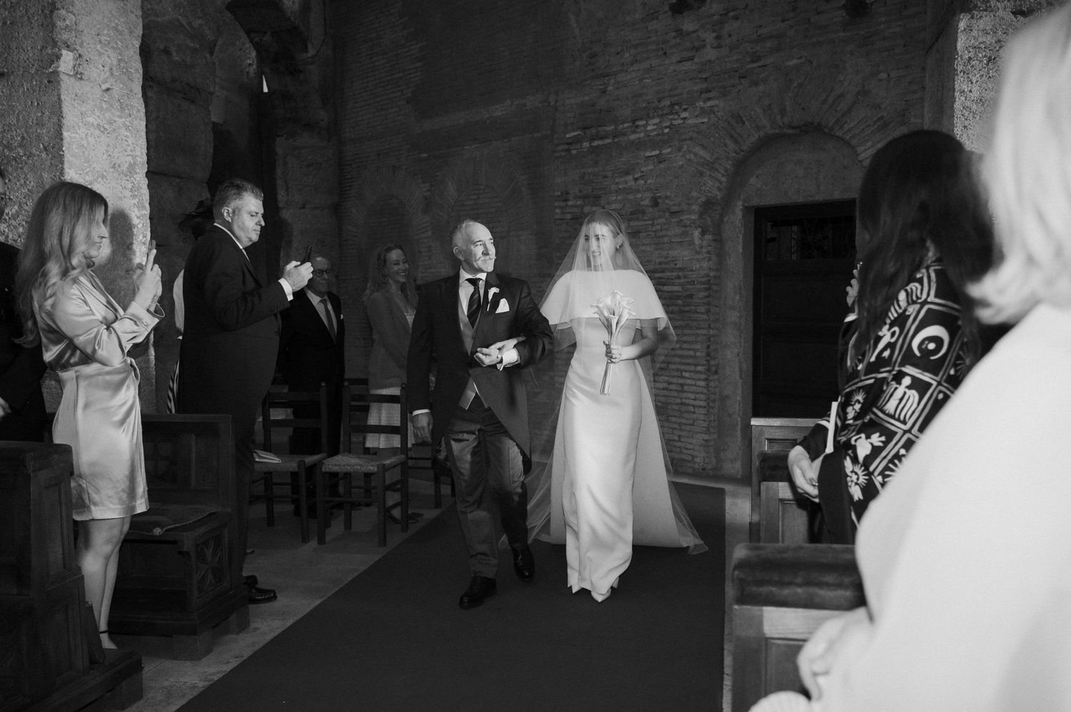 Wedding ceremony procession in a historic brick venue with arched architecture.