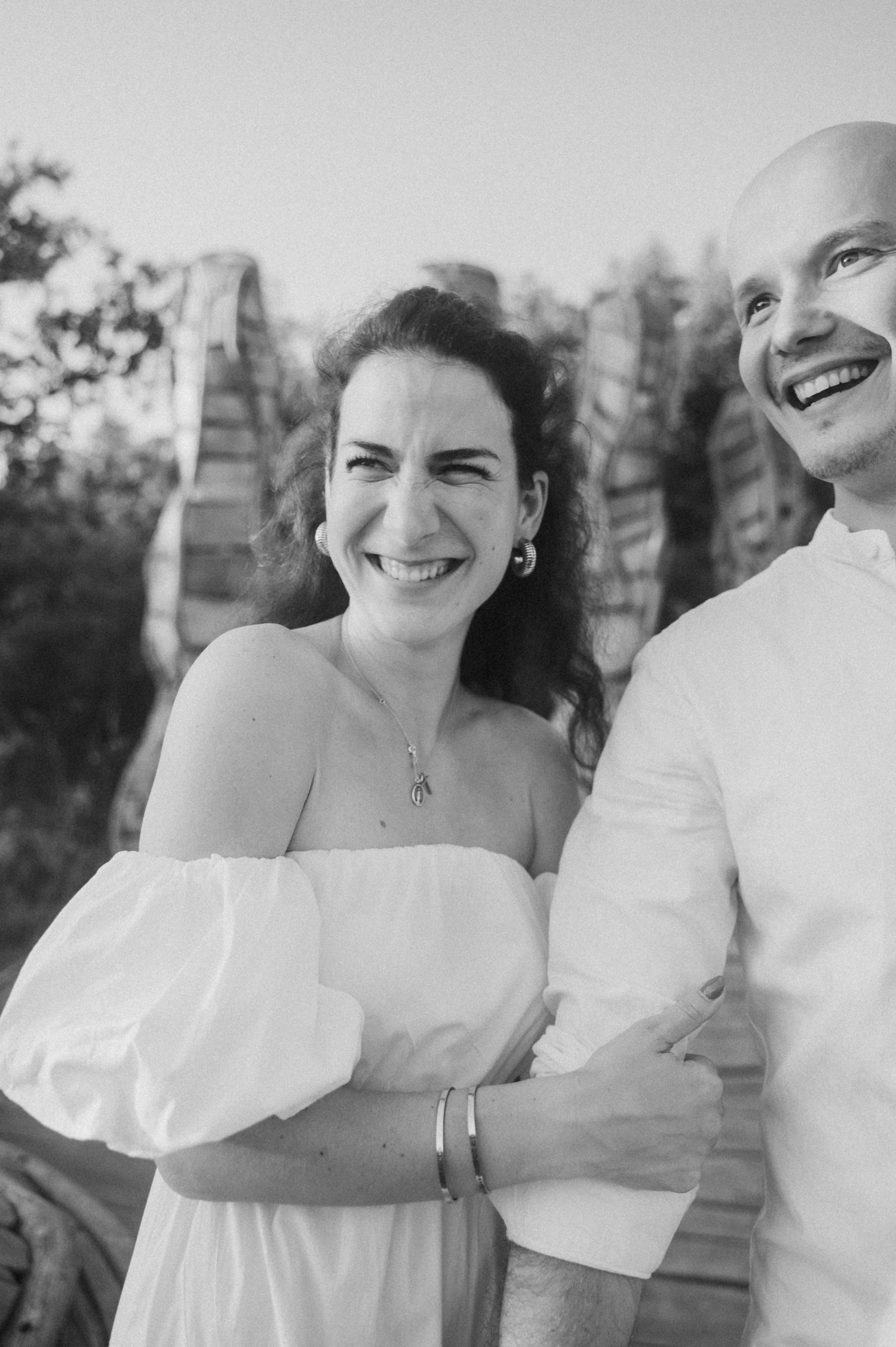 A series of black and white candid photos showing joyful moments between a couple in white attire outdoors.