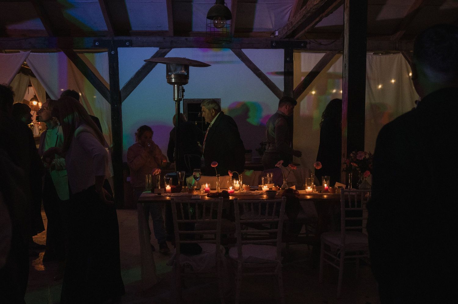 Guests dance and celebrate at an evening wedding reception under string lights and rustic wooden beams.
