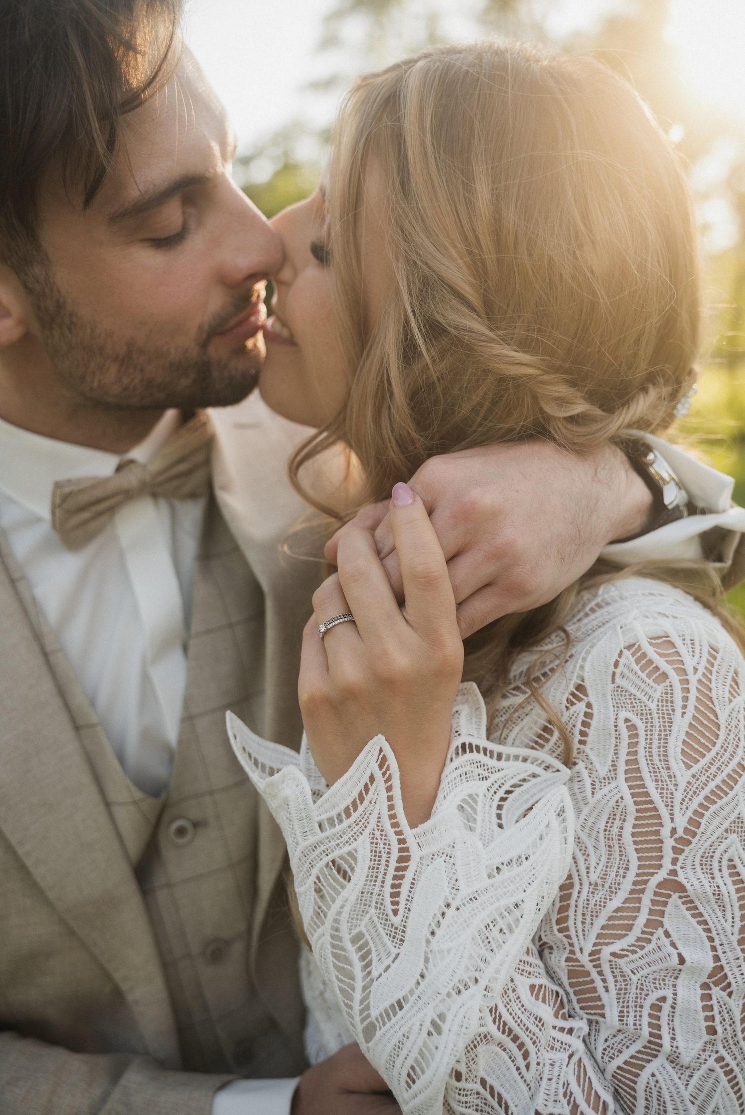 Newlyweds share intimate moments in golden sunlight wearing elegant wedding attire.