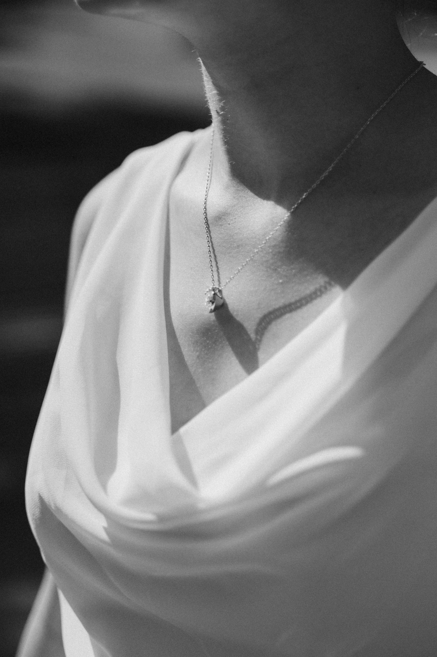 Black and white close-up of a delicate necklace chain against white fabric creating an elegant minimalist composition.