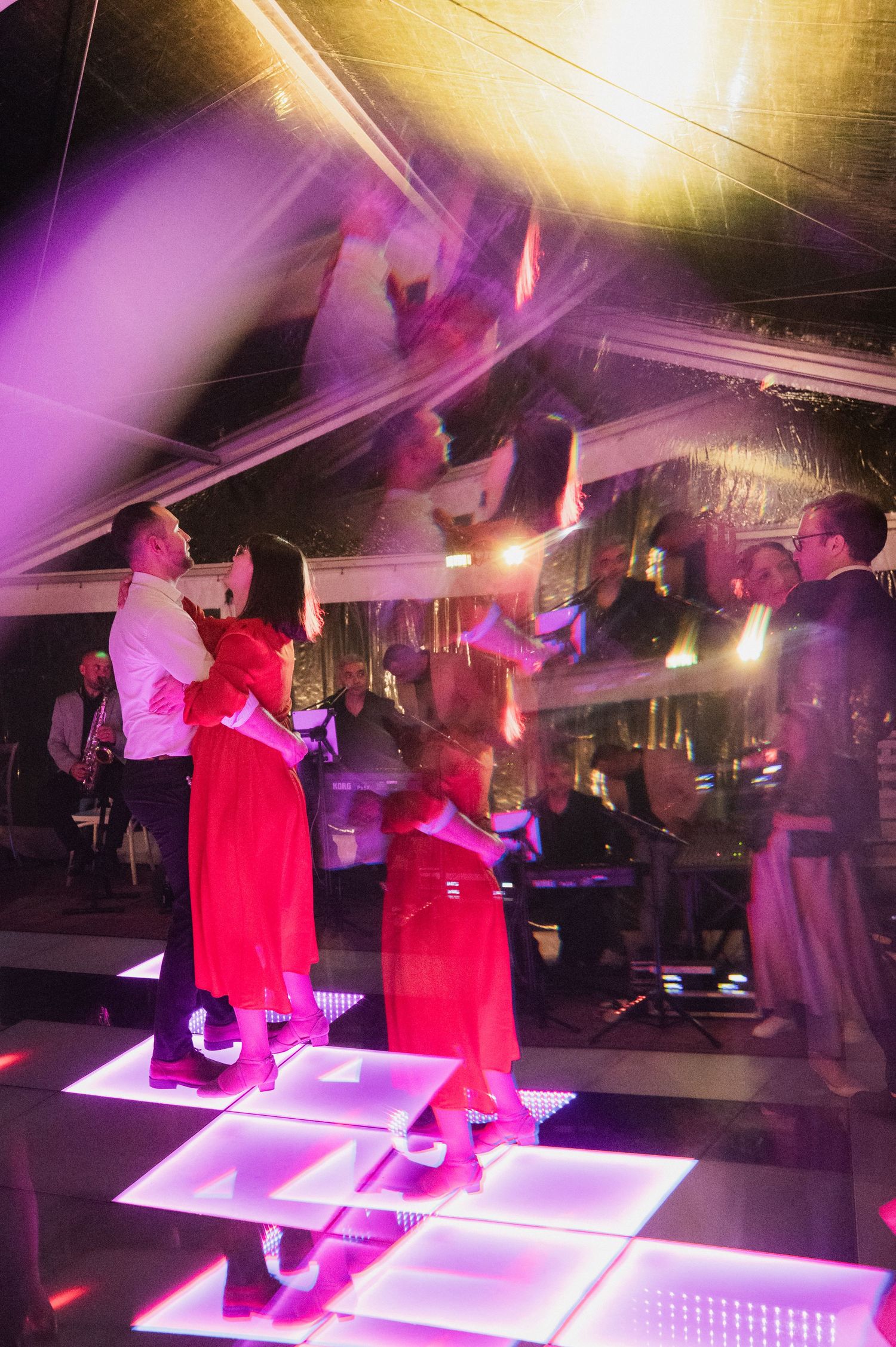 Wedding guests dancing on illuminated LED dance floor under colorful pink and purple lights at reception.