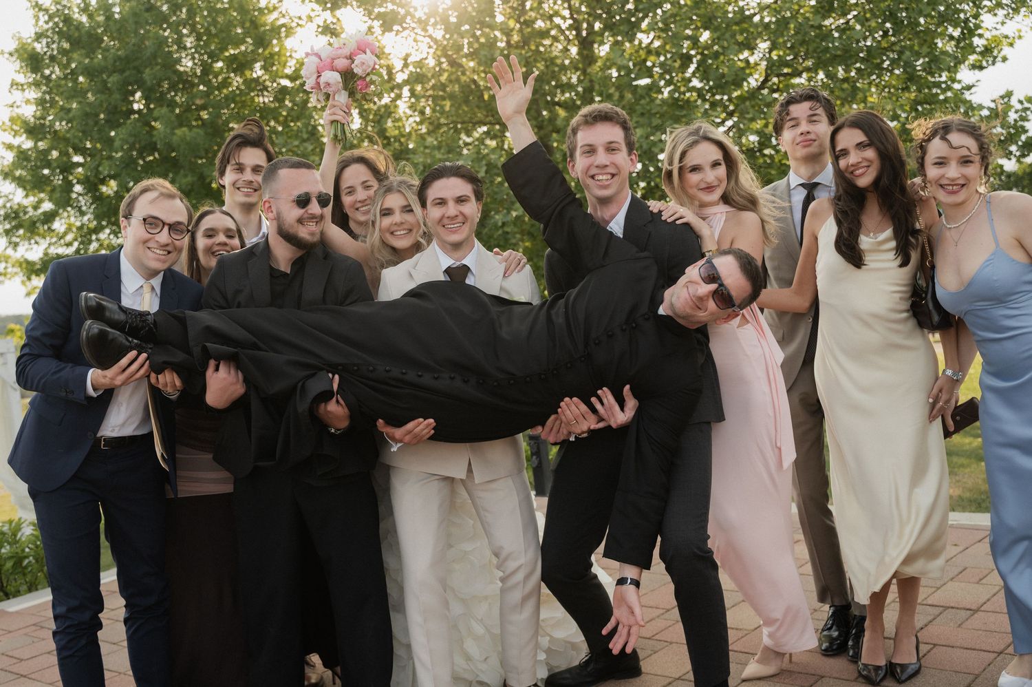 Joyful wedding party lifting a guest horizontally in a fun outdoor group celebration photo.
