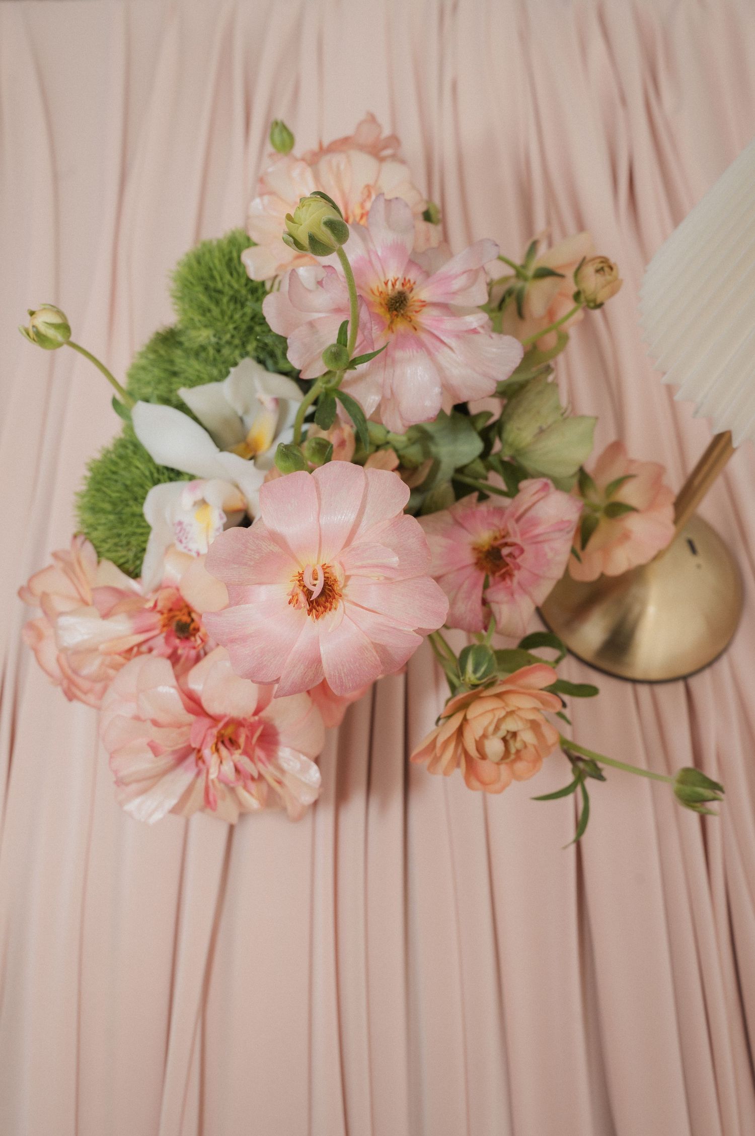 Elegant wedding bouquet of pink dahlias, ranunculus, and green flowers on soft blush pink fabric.