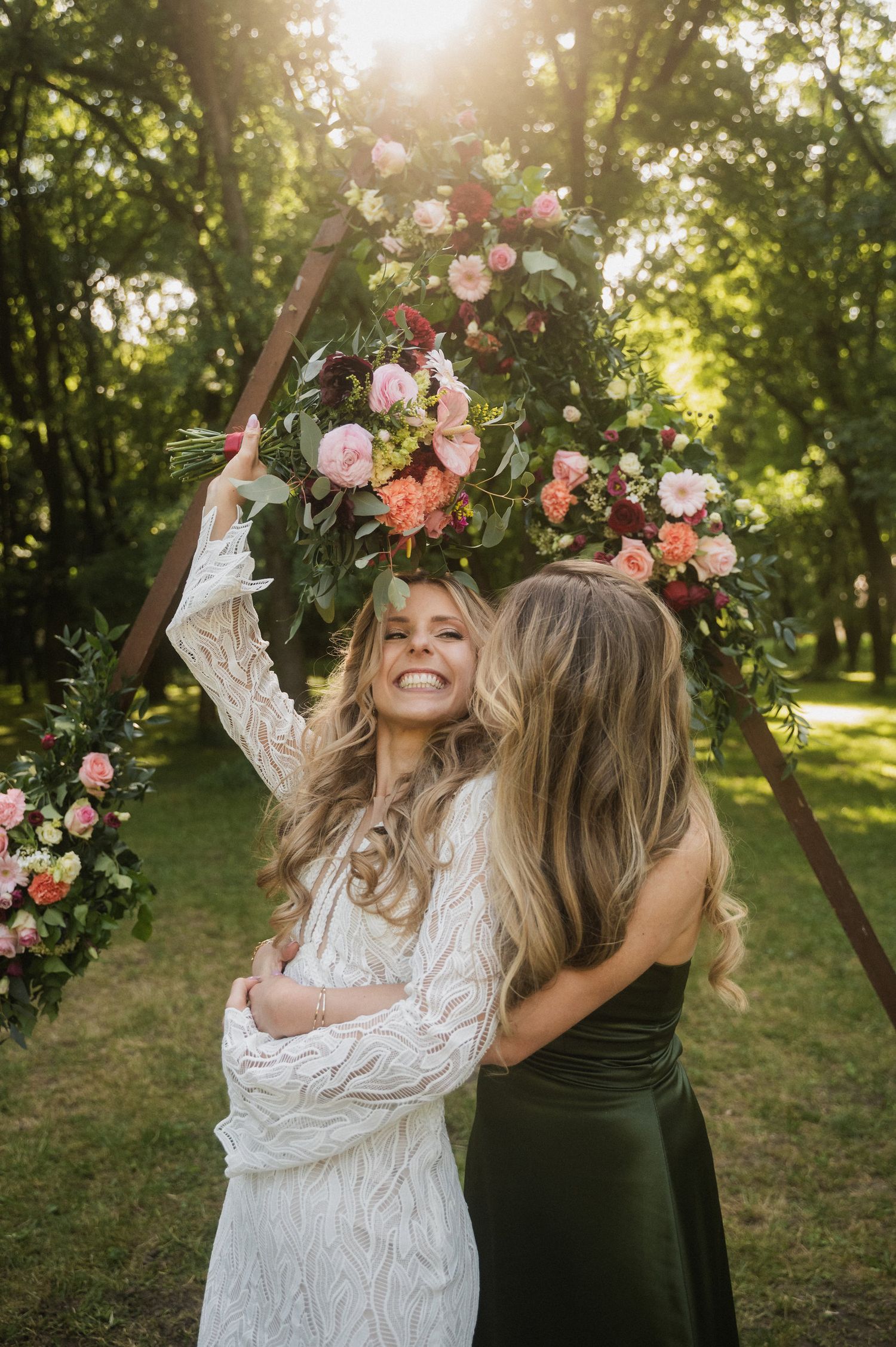 Two friends wearing floral crowns dance and laugh together in a sunlit garden setting with pink roses.