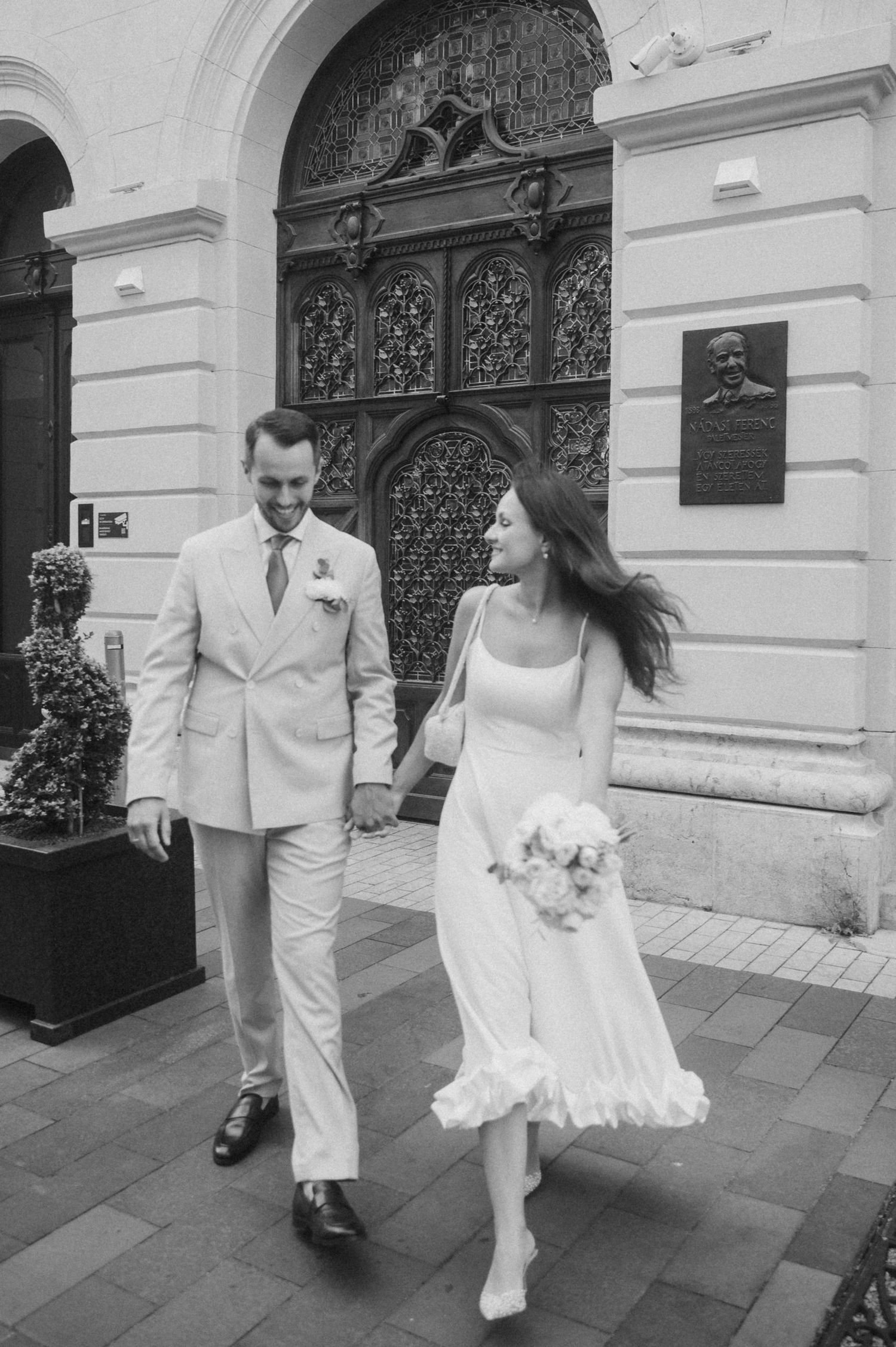 Black and white sequence of newlyweds dancing along an elegant building facade.