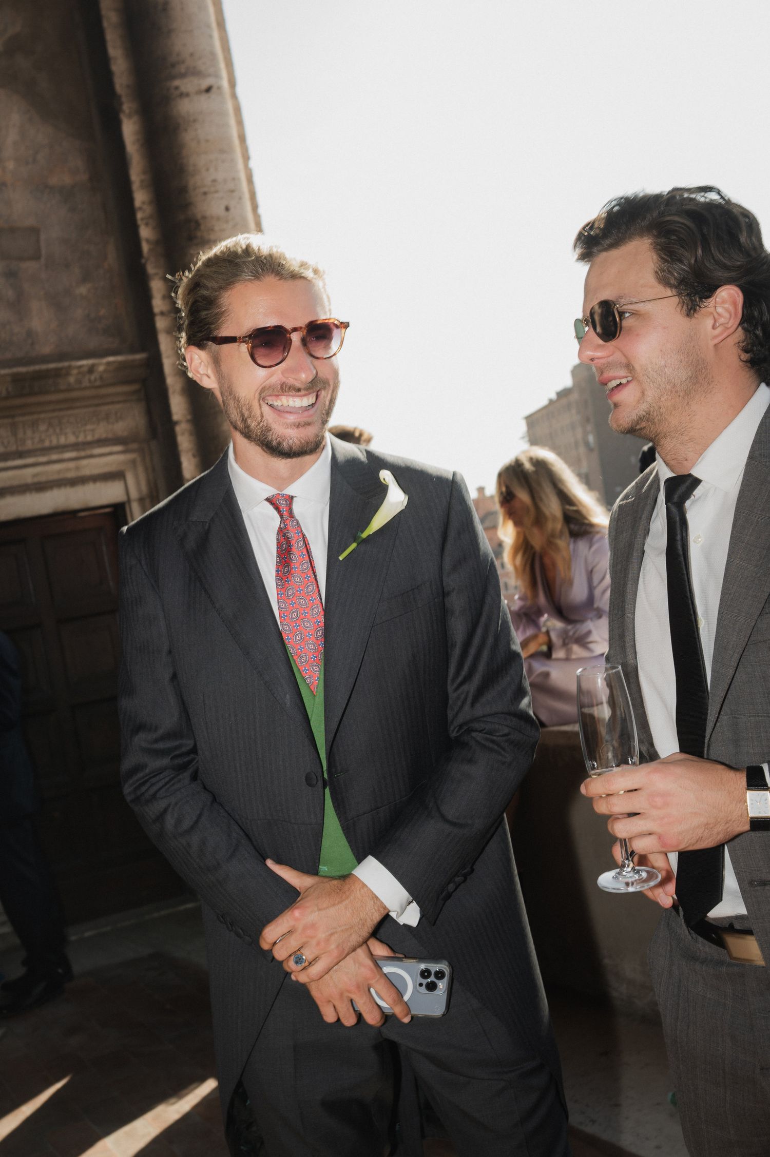 Guests in formal attire share laughs during an outdoor wedding reception.