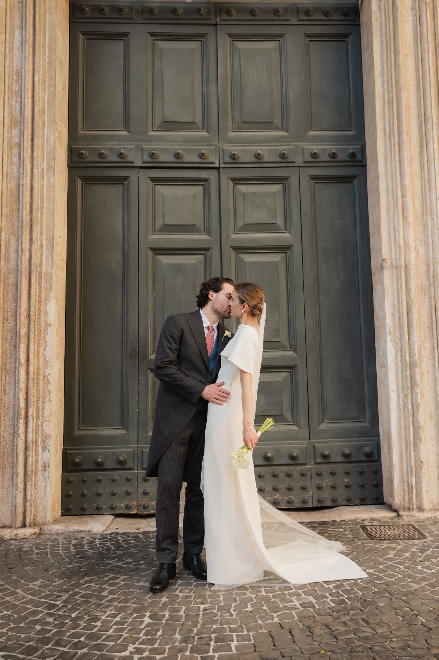 Intimate wedding moment captured in front of grand historic doors with stone columns.