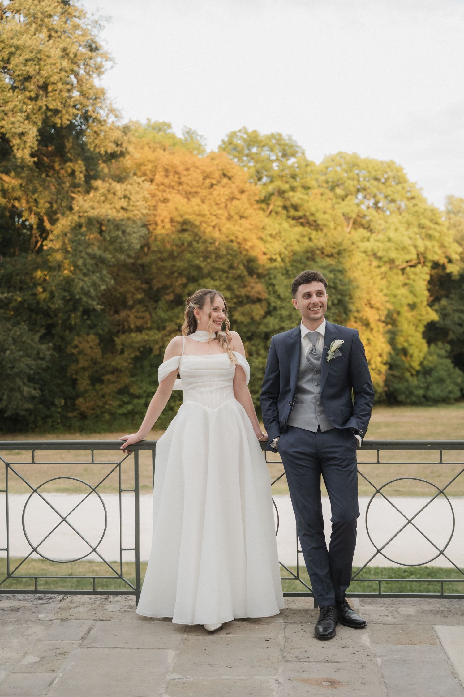 Bride and groom pose together on a terrace surrounded by autumn trees in golden foliage.