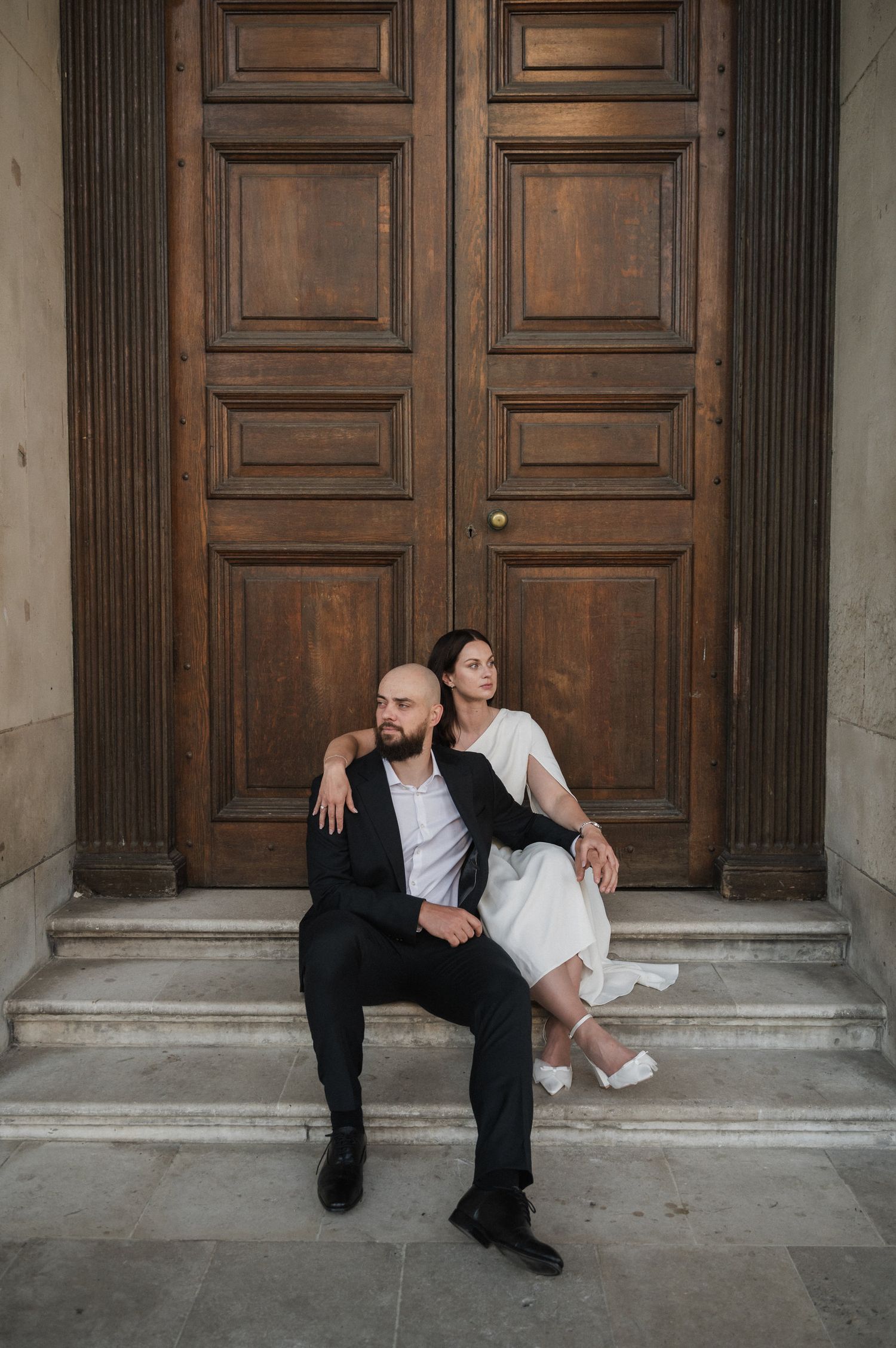 Wedding couple creates dynamic poses in front of classic architectural columns and doors.
