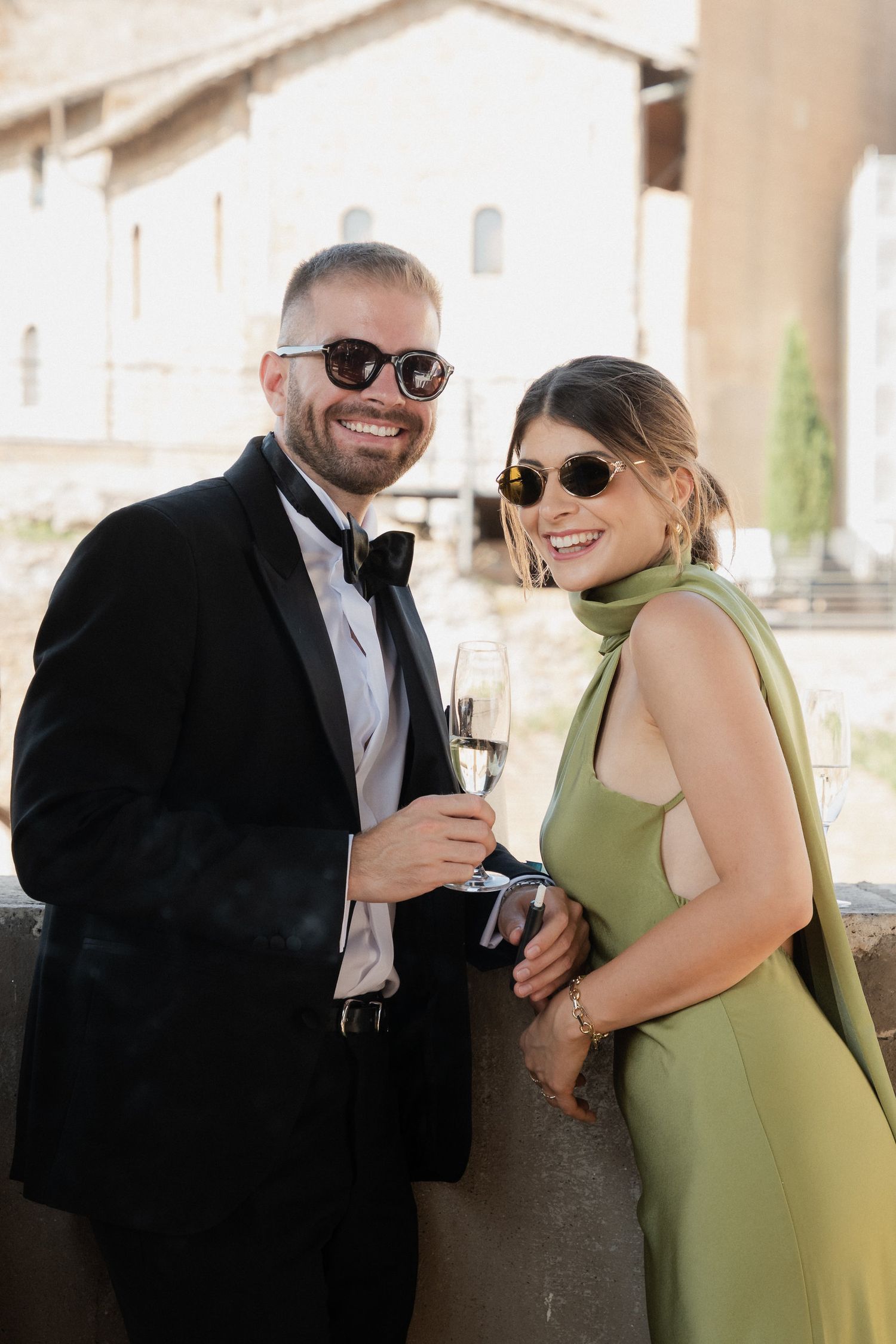 Wedding guests in formal attire share laughs under stone archways during reception.