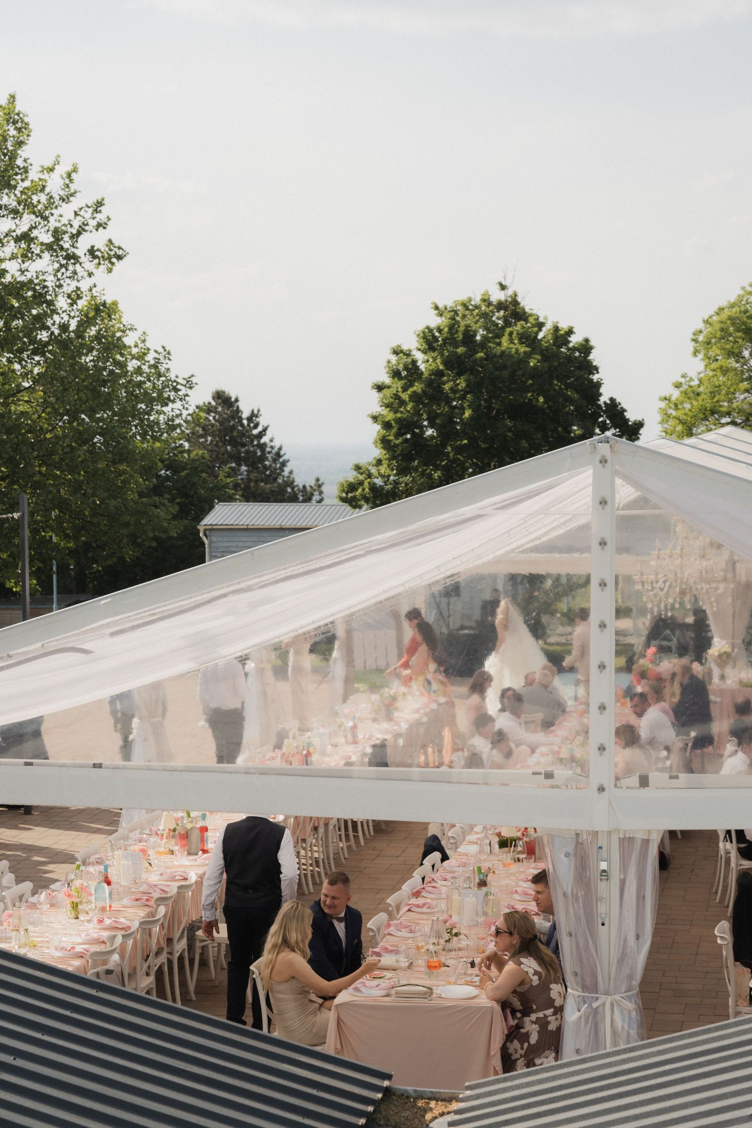 Aerial view of a wedding reception under a clear marquee tent with long decorated dining tables.