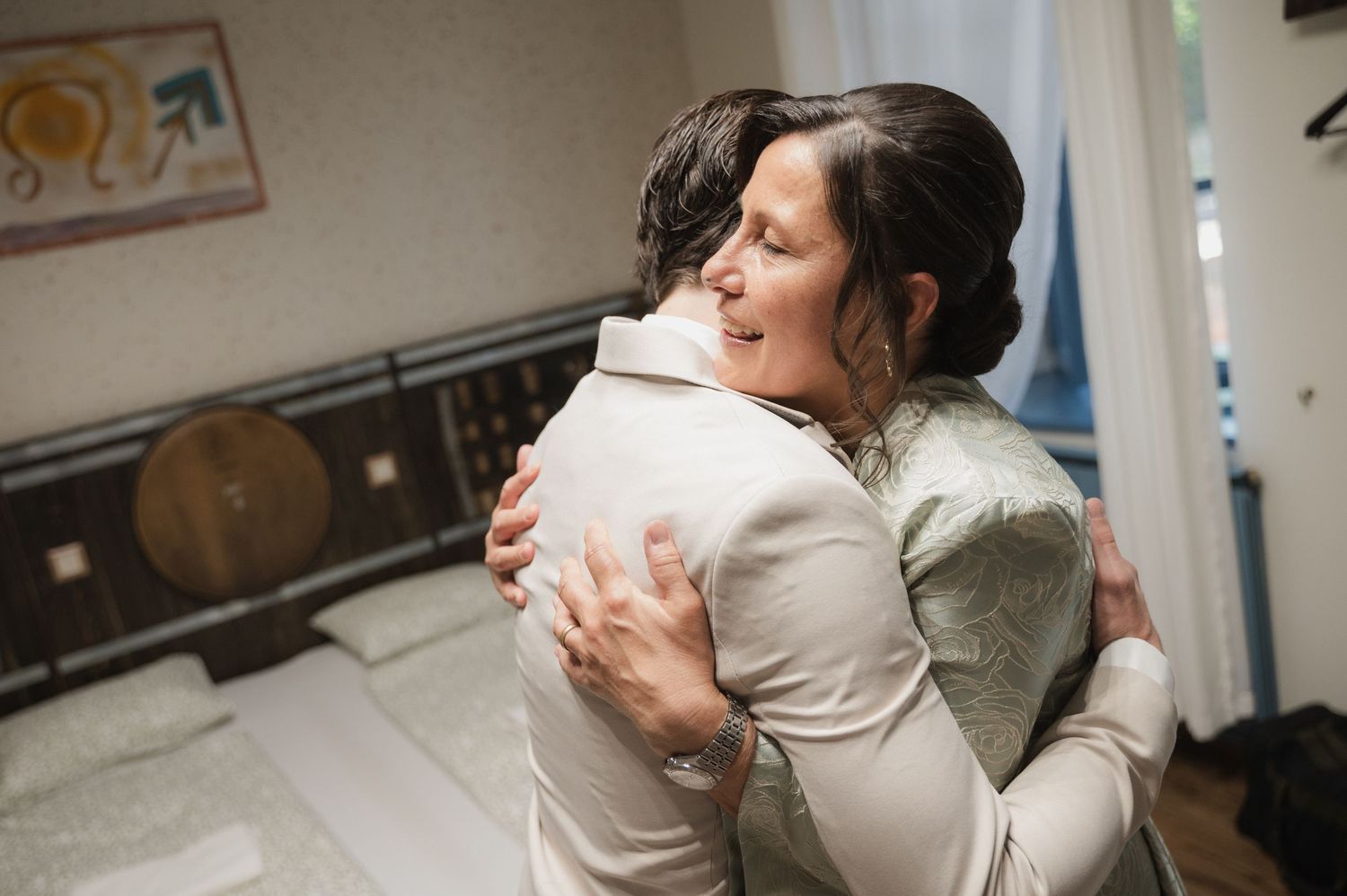 Two women share a warm embrace in a bedroom during wedding preparations.
