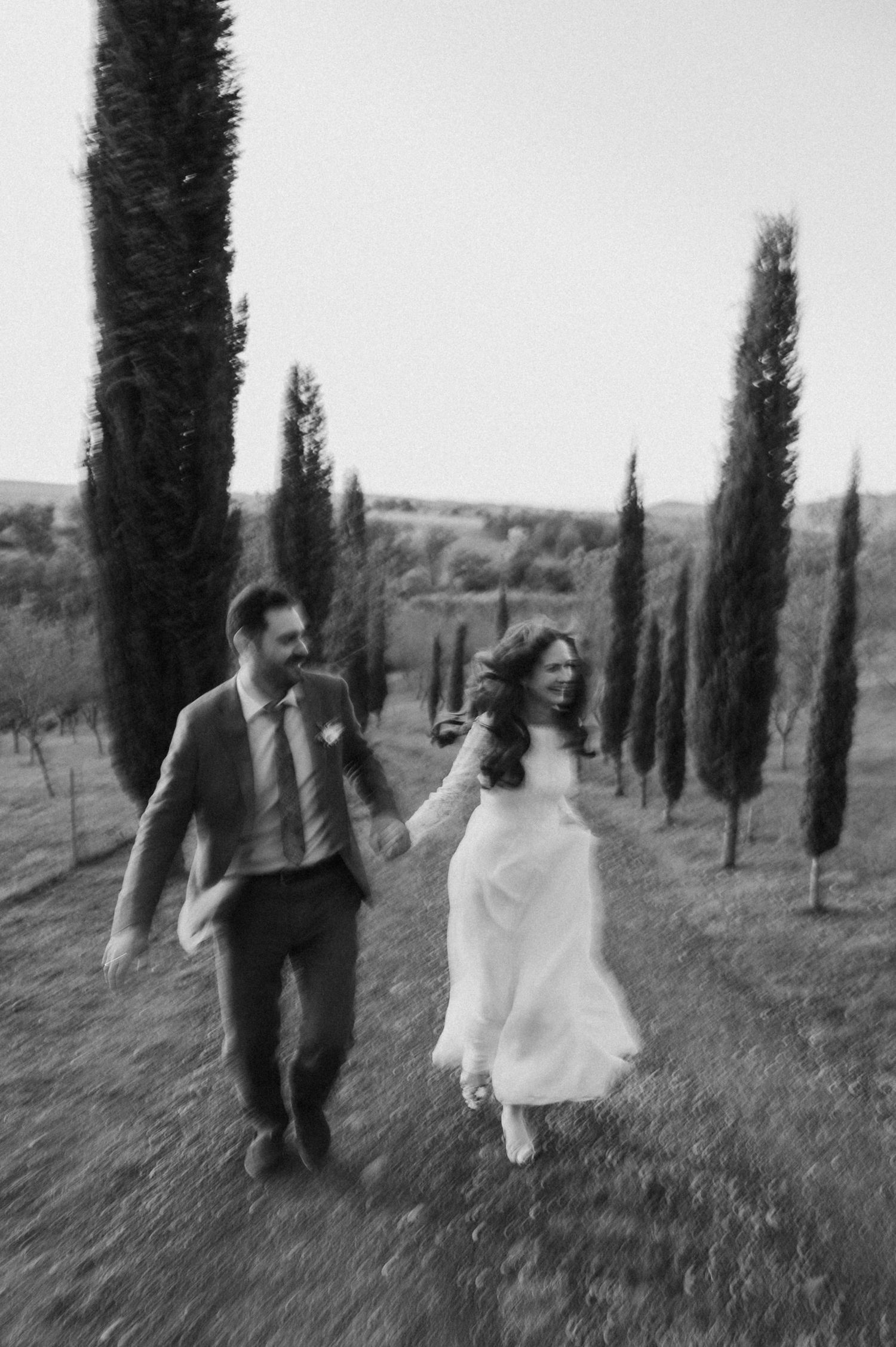 Black and white romantic photo sequence of a couple walking through a cypress tree-lined path in Tuscany.