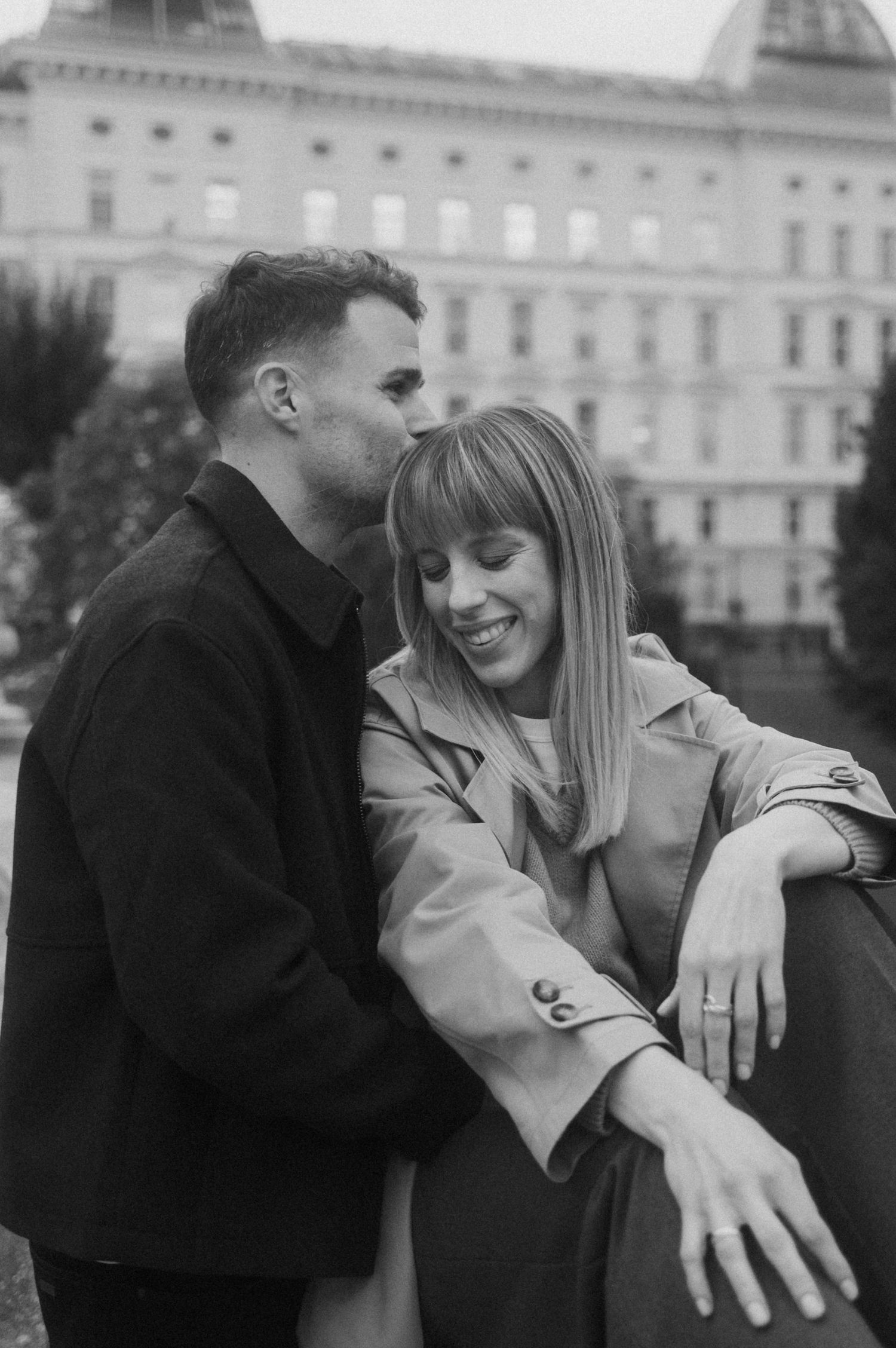 A romantic black and white portrait of a couple sharing an intimate moment in front of a grand historic building.