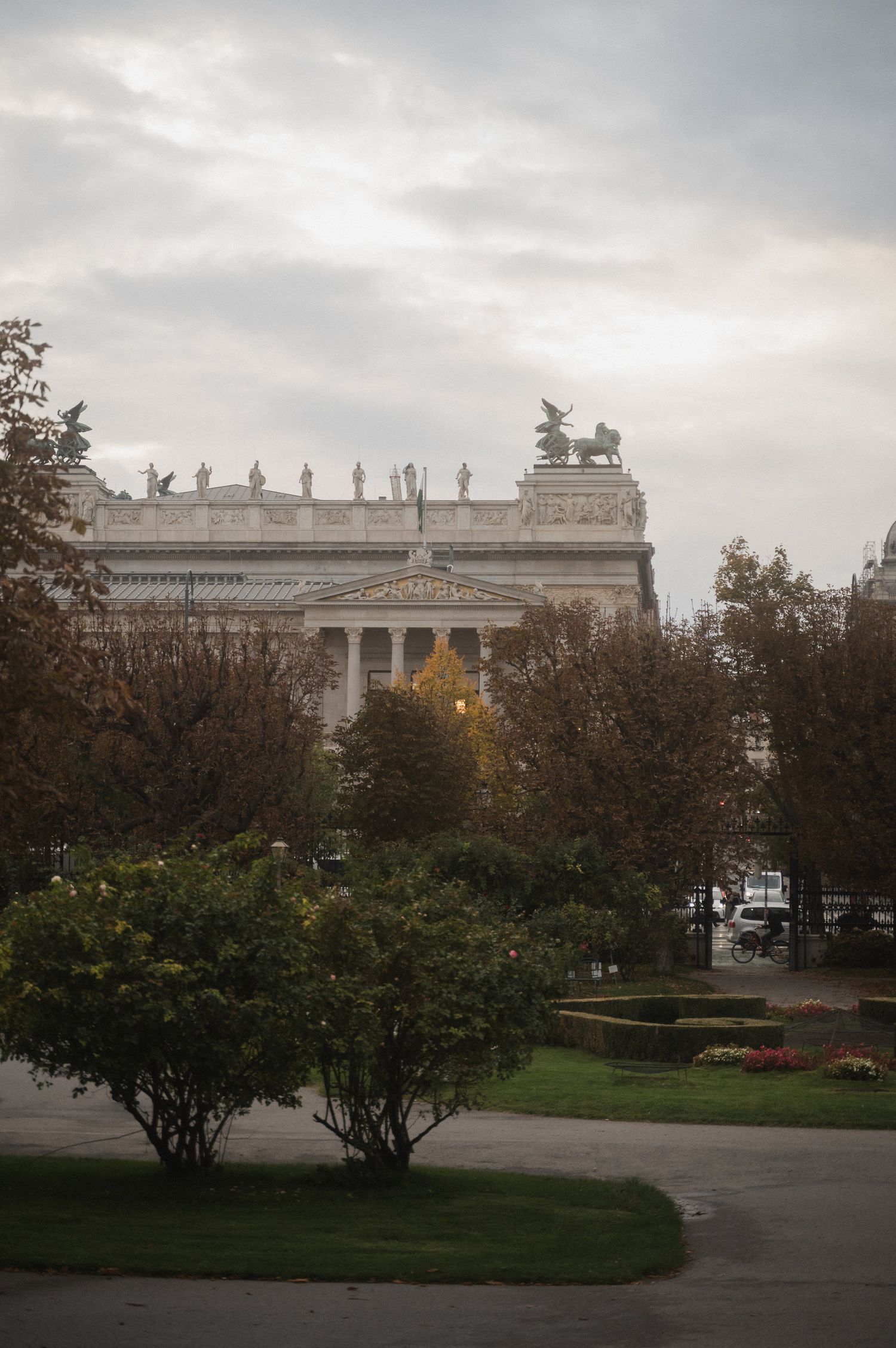 Neoclassical building with white columns and ornate architecture seen through autumn trees in an urban park setting.