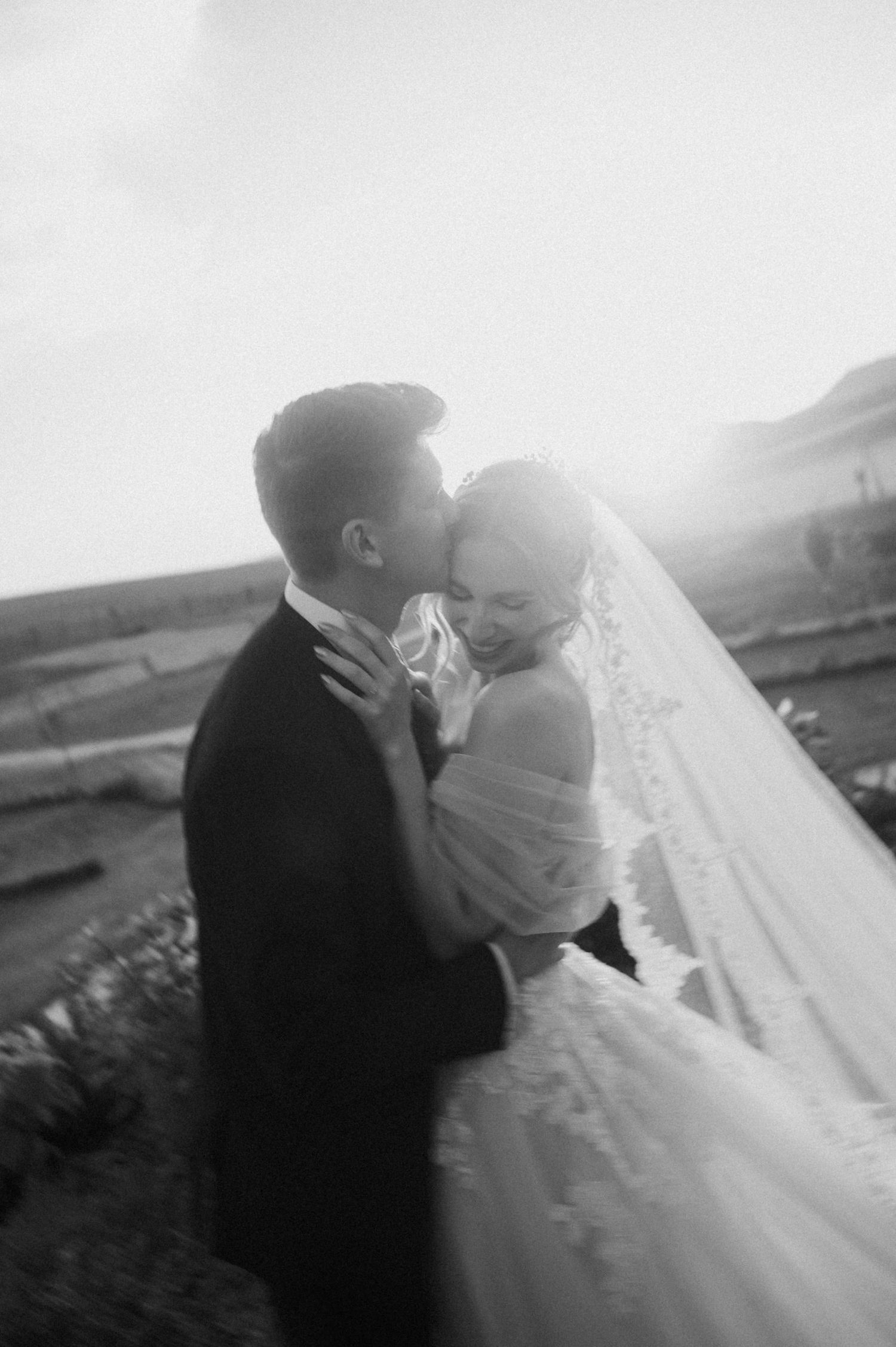 Black and white portrait of newlyweds sharing intimate moment at sunset.