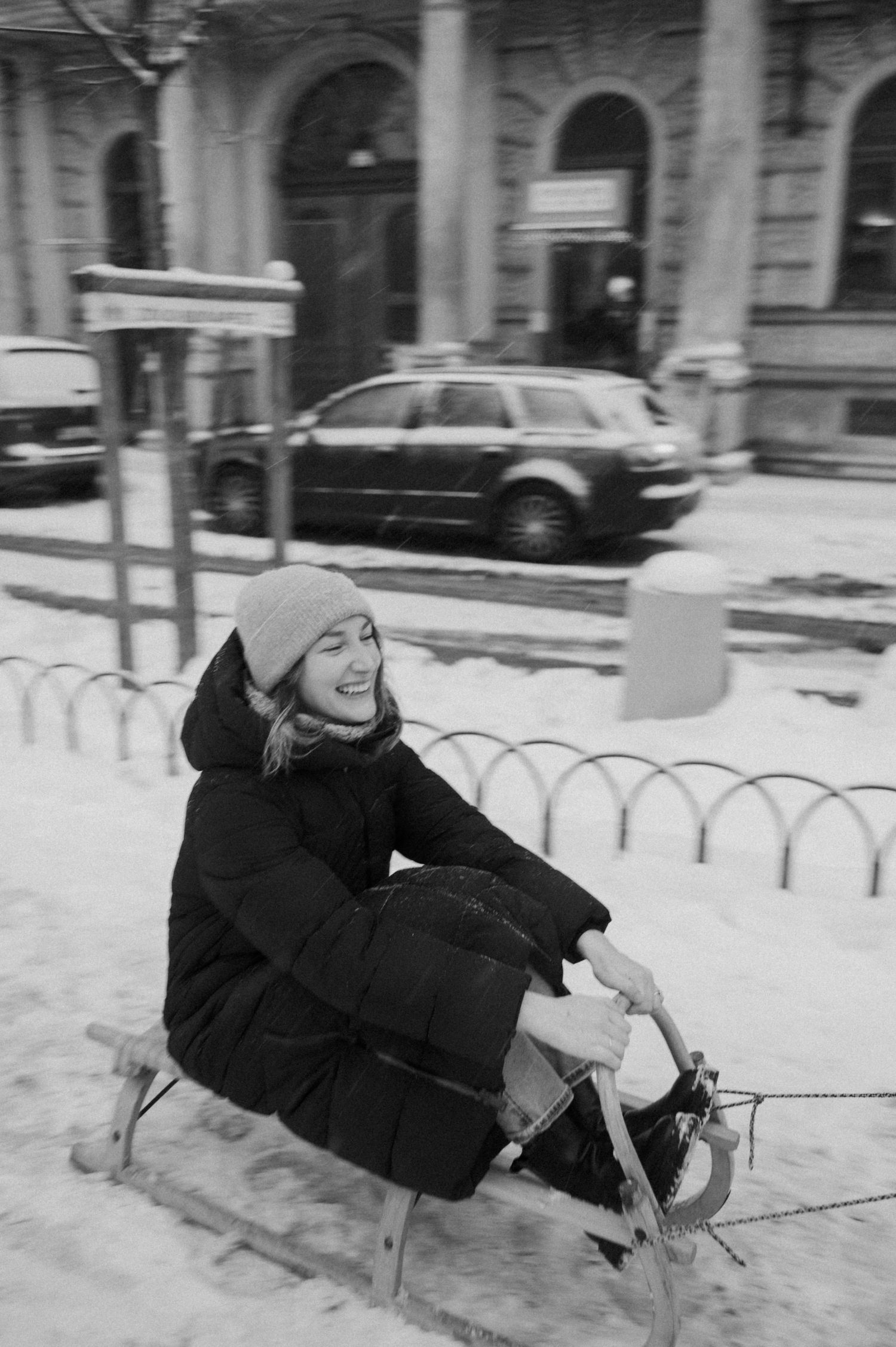 Someone riding a wooden sled in the snow near a historic building.