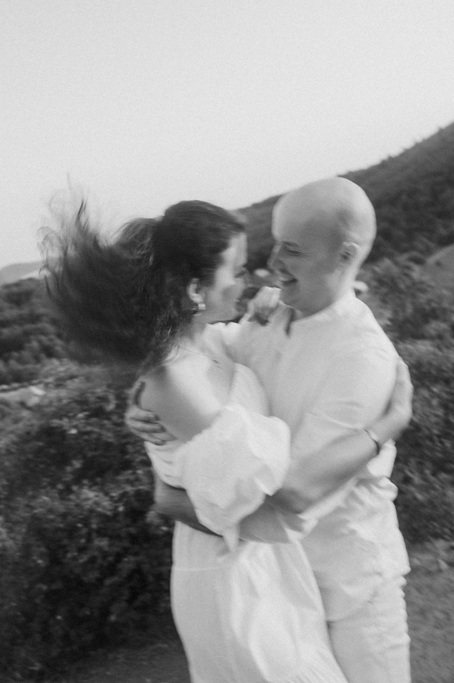 A sequence of black and white photos showing a couple in white clothing embracing and dancing outdoors in nature.