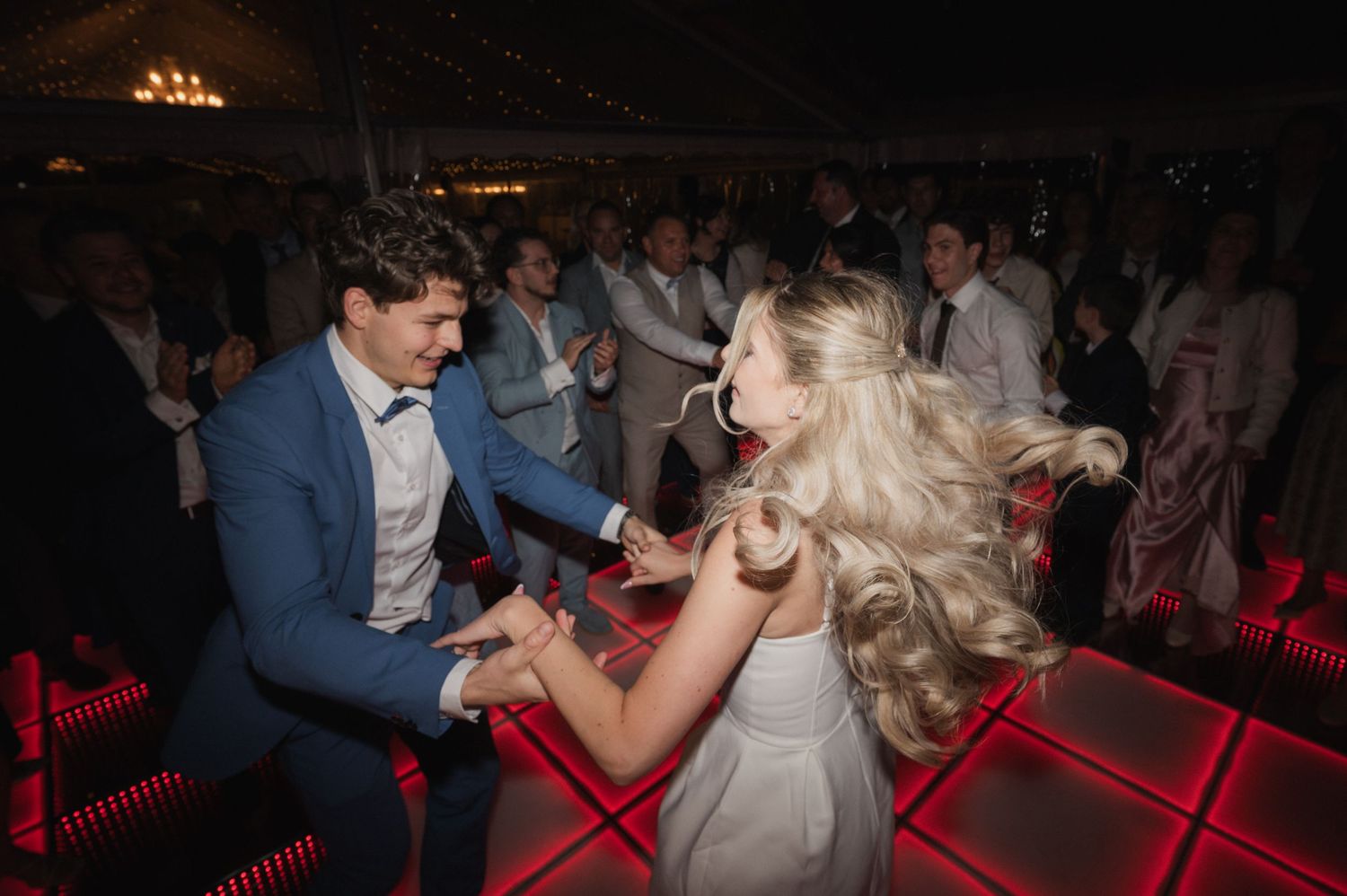 Bride and groom dance energetically together on a glowing red dance floor at their wedding reception.