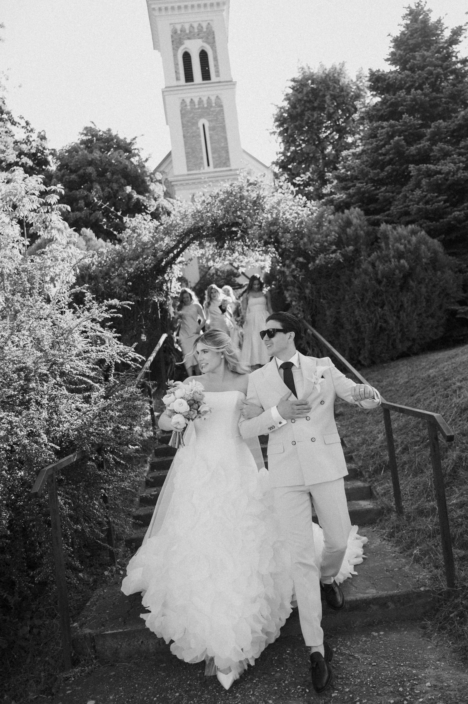 Black and white photo of bride and groom descending church steps after wedding ceremony.