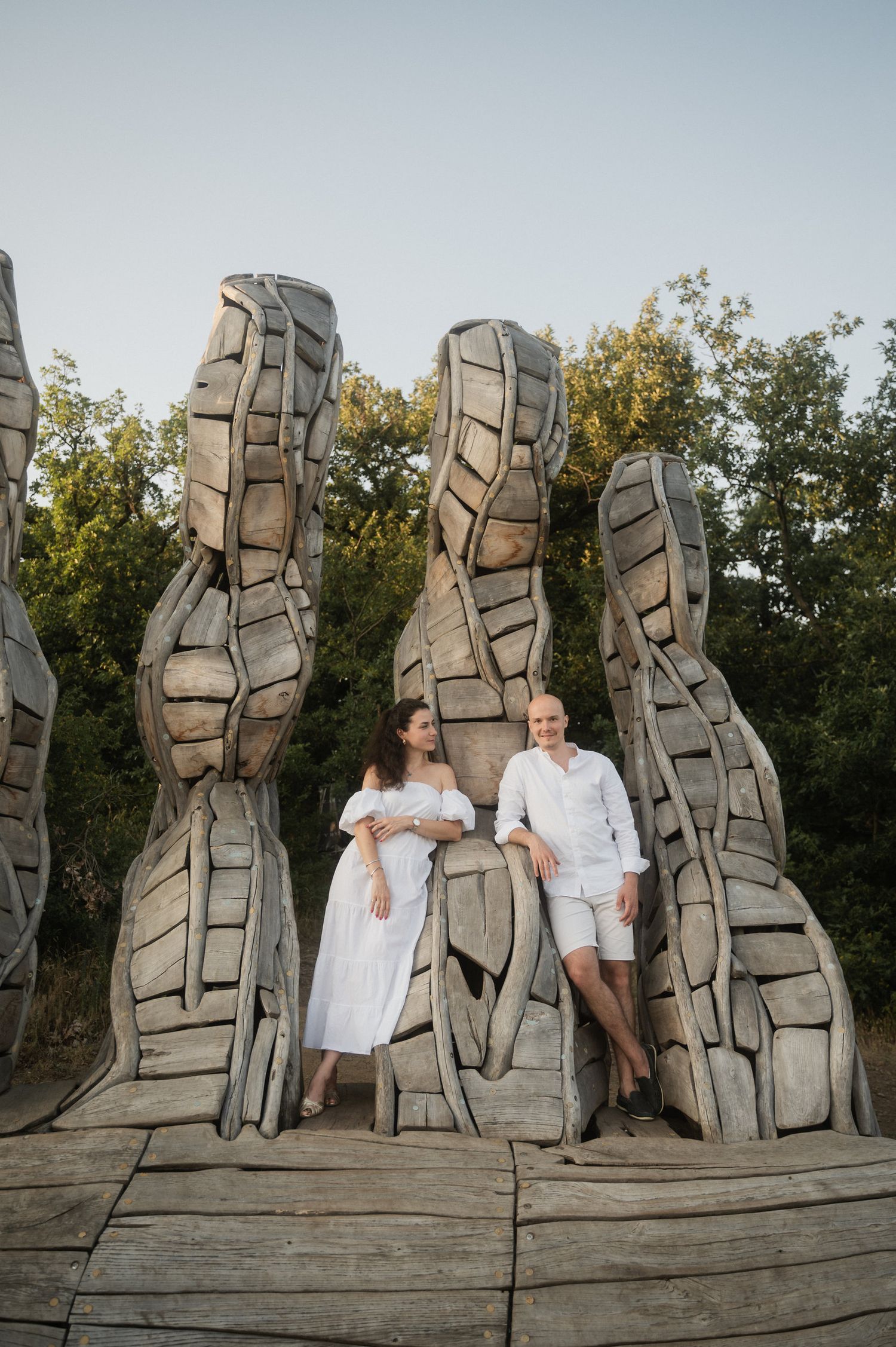 A couple poses together at a modern stone sculpture installation in a natural outdoor setting during golden hour.