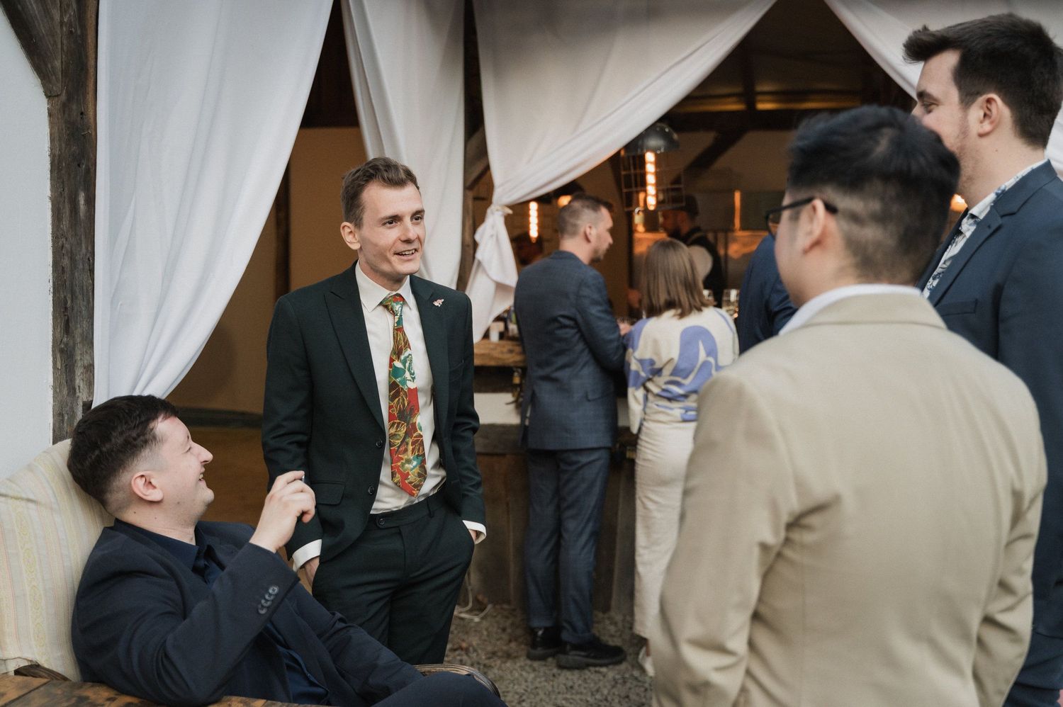 Wedding guests gather under an elegant white tent canopy during an outdoor reception celebration.