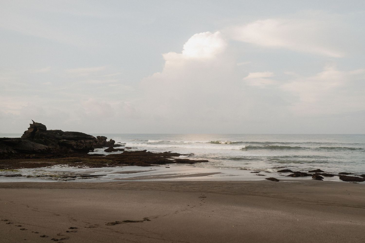 A scenic coastal landscape with rocky outcrops and waves crashing against the shore under an overcast sky.